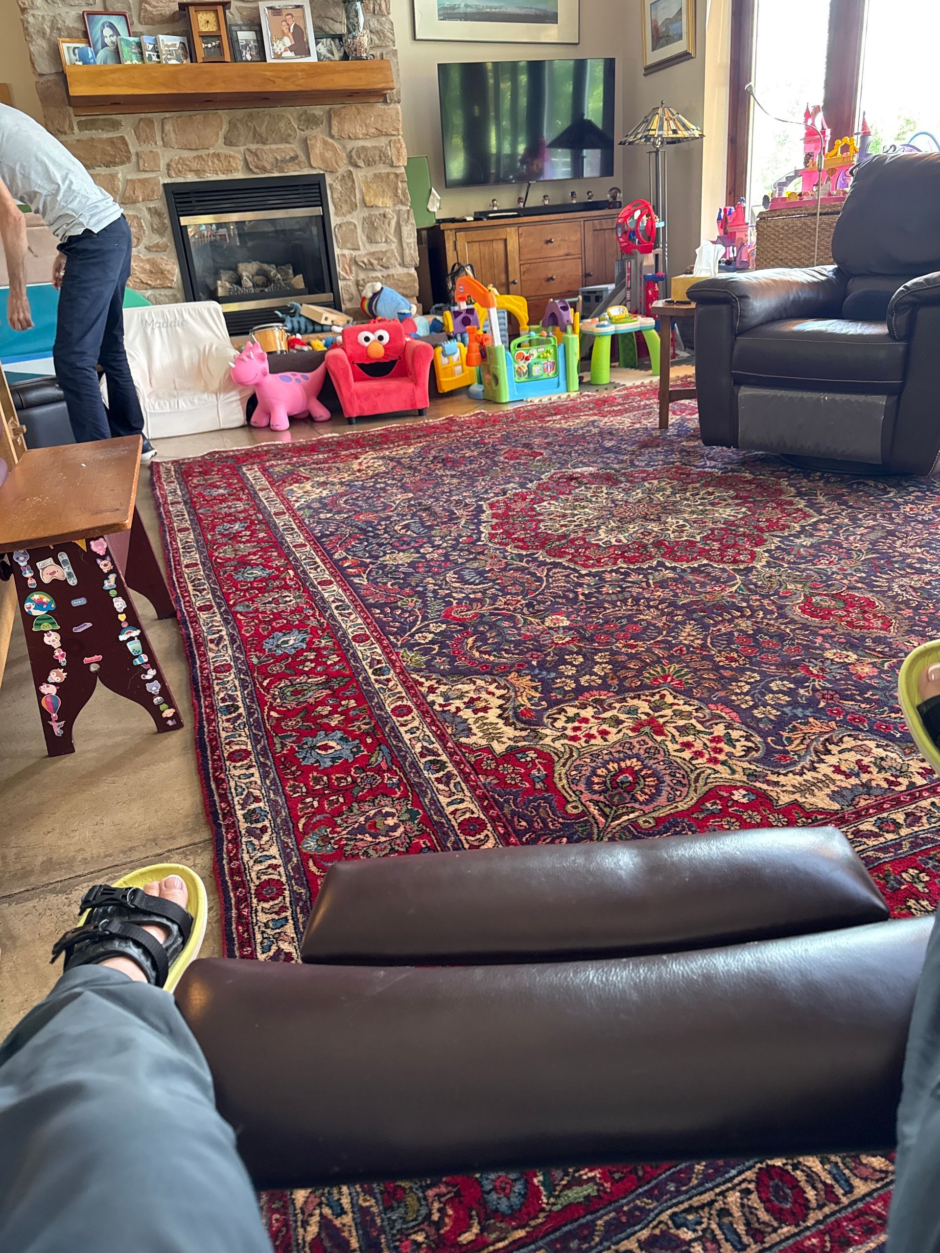 Person in recliner views living room with fireplace, toys, and oriental rug.