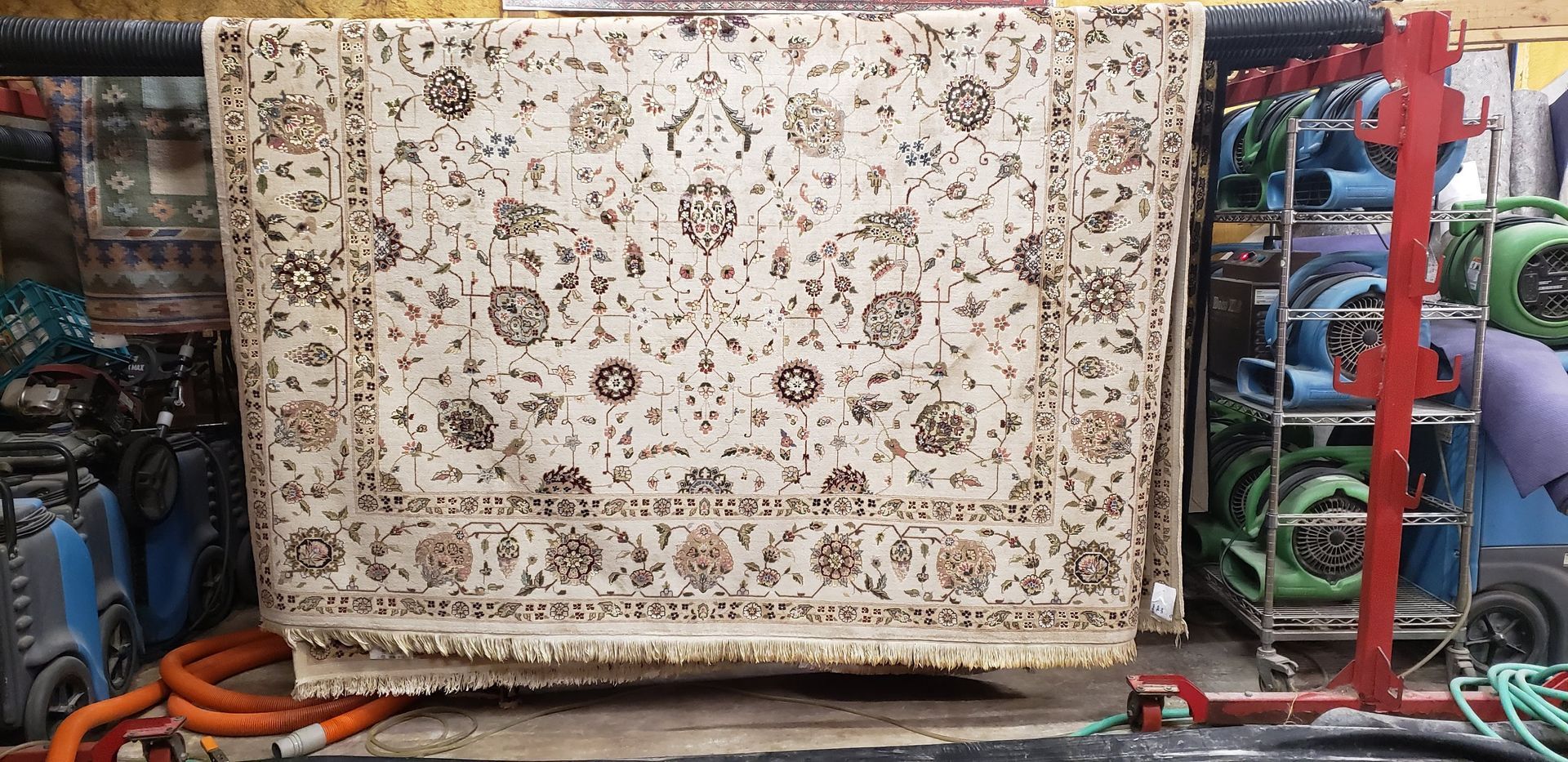 Beige rug with floral pattern hanging in what appears to be a cleaning facility.