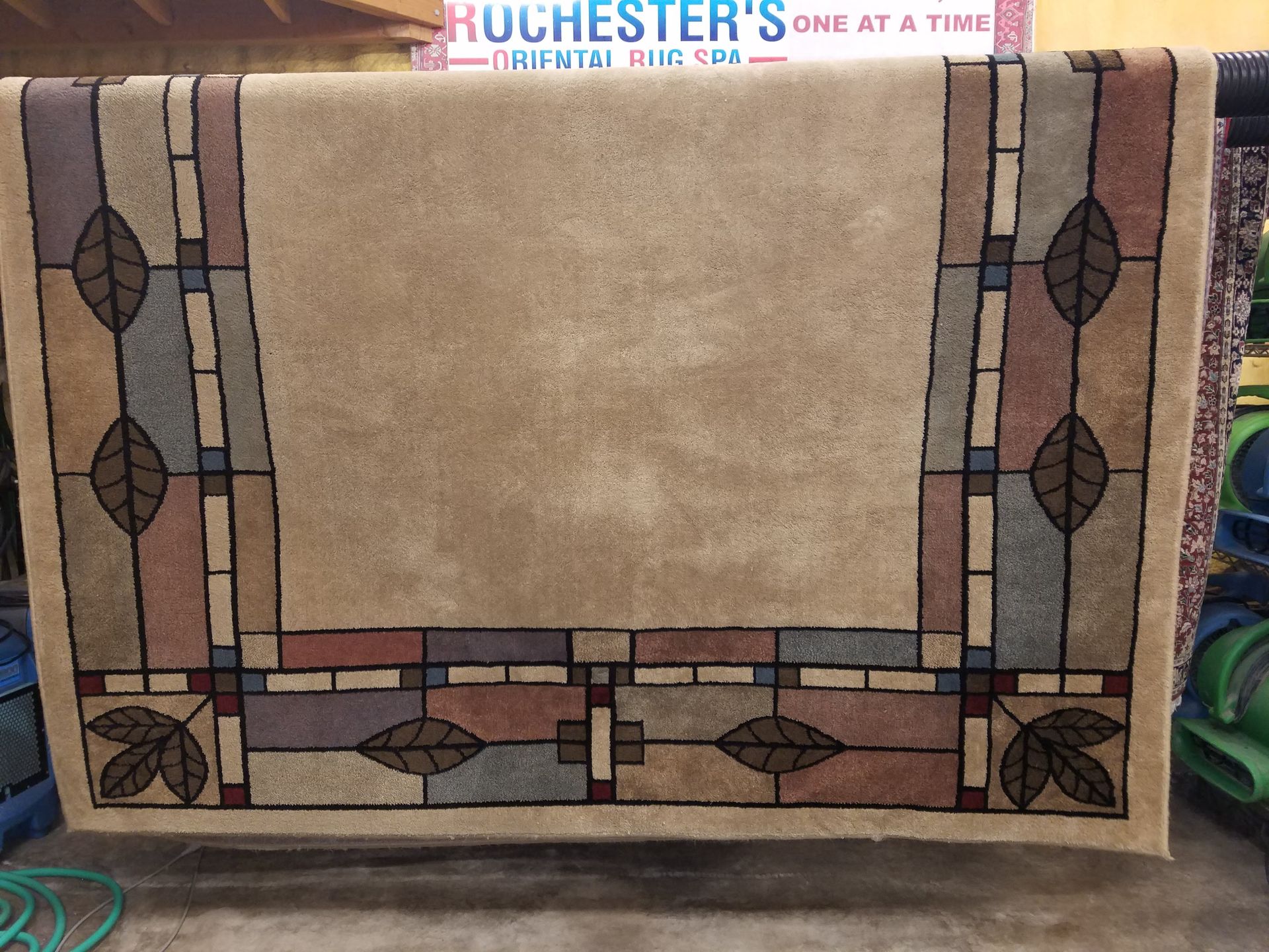 Beige rug with a brown and tan geometric border featuring leaf motifs.