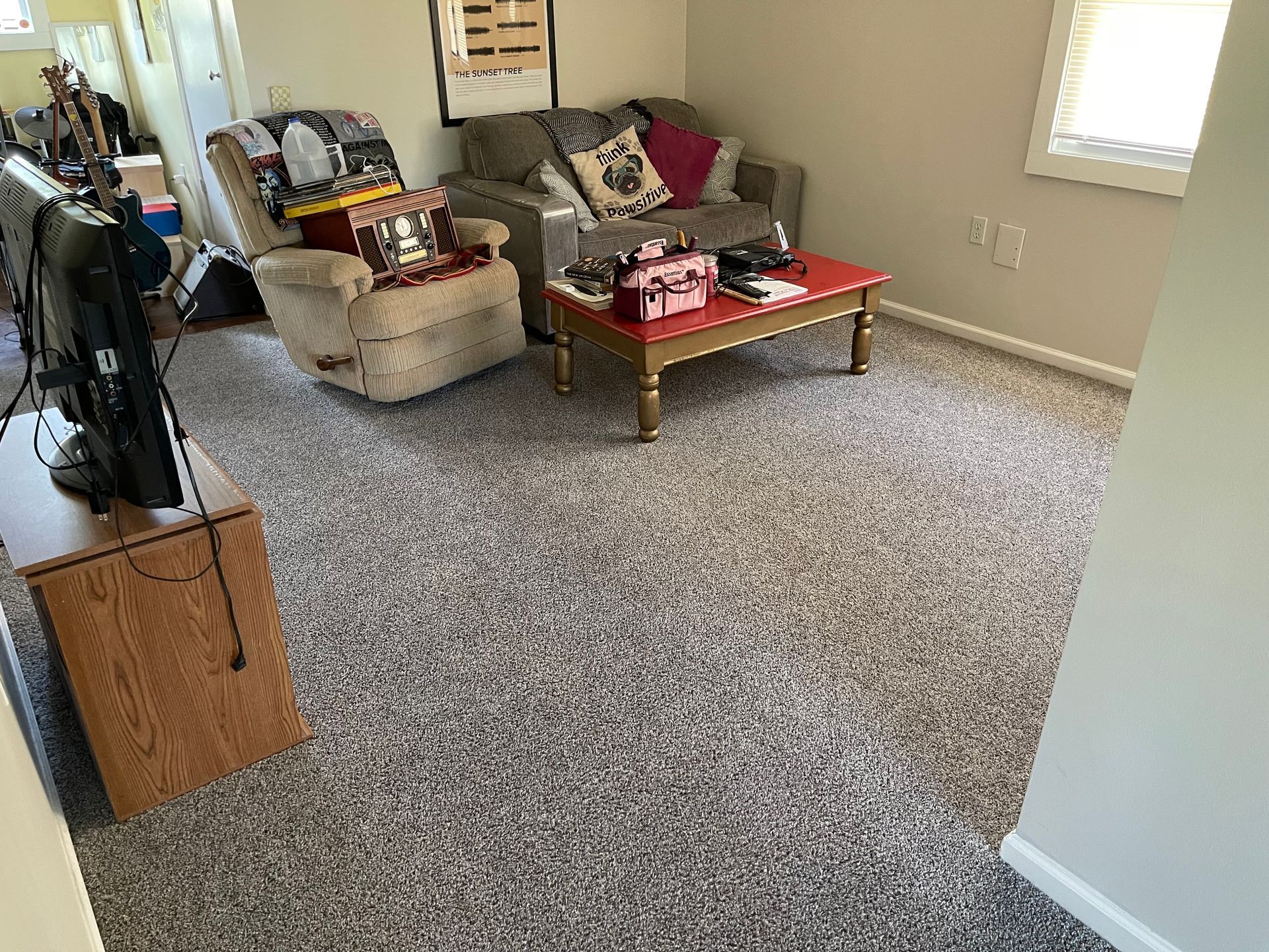 Living room with gray carpet, sofa, recliner, coffee table, and TV on a wooden stand.