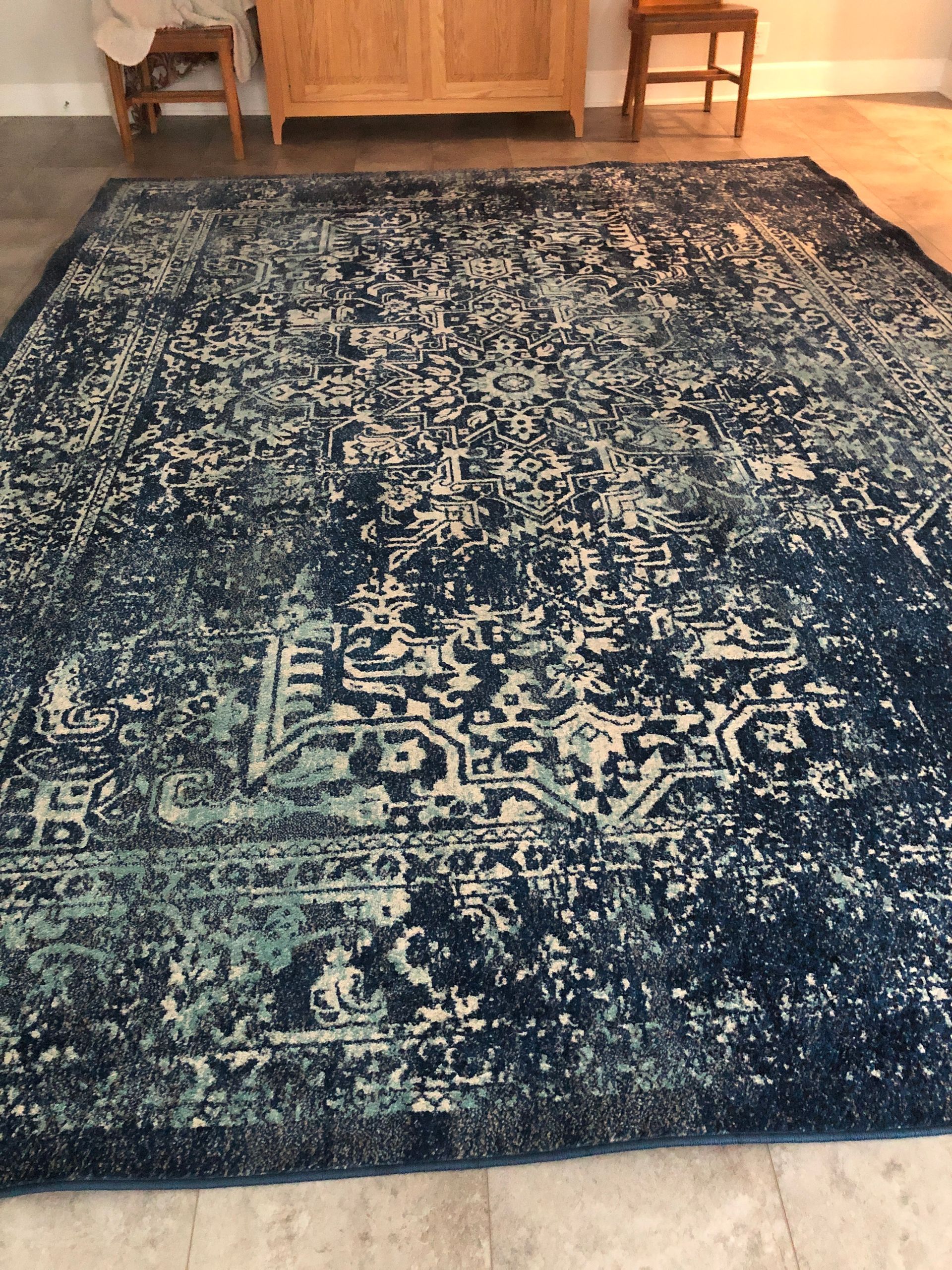 Blue and ivory distressed patterned rug on a light floor, with wooden furniture in the background.
