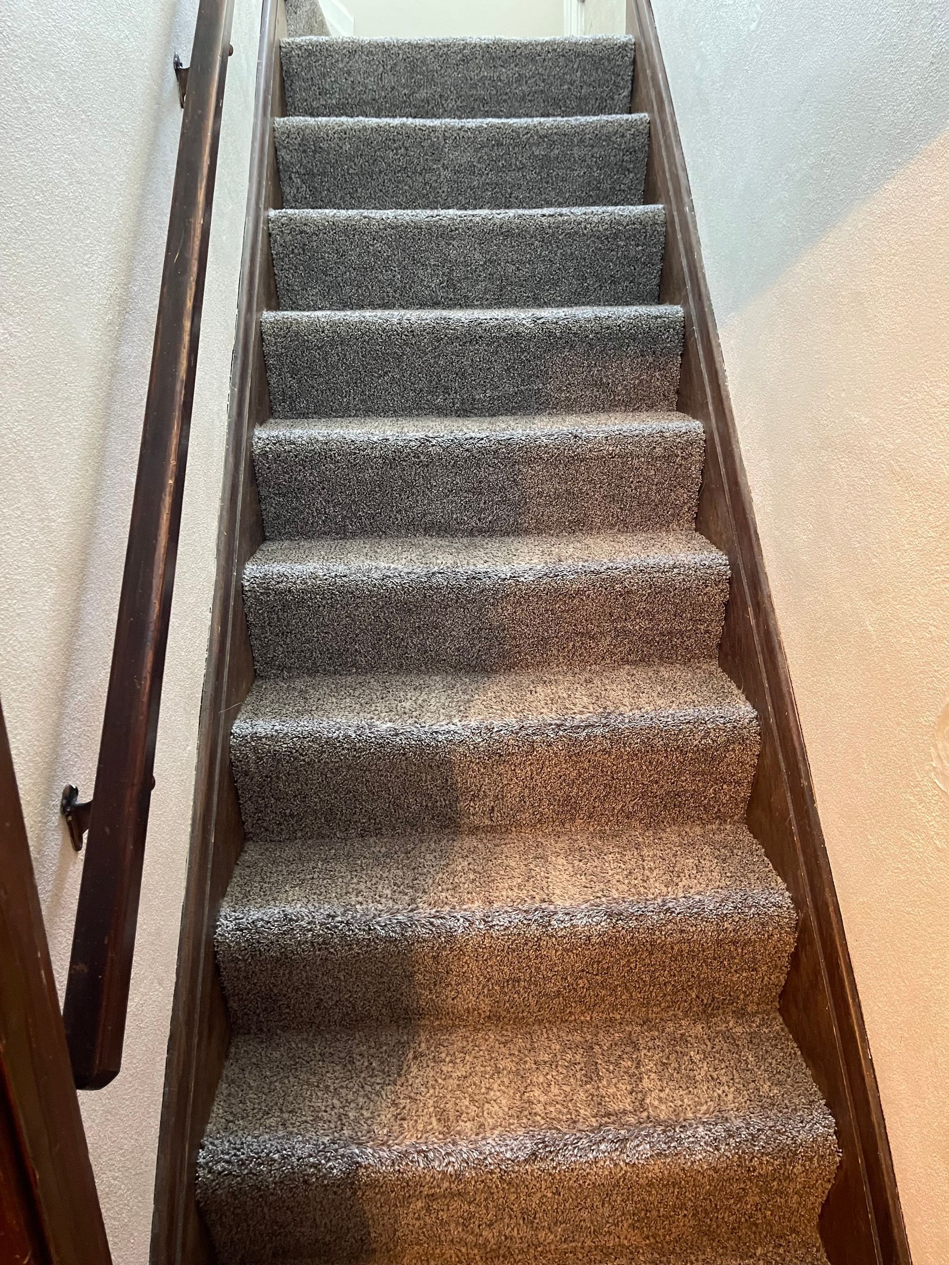 Carpeted staircase with wooden handrail on the left. Light gray carpet, beige walls.