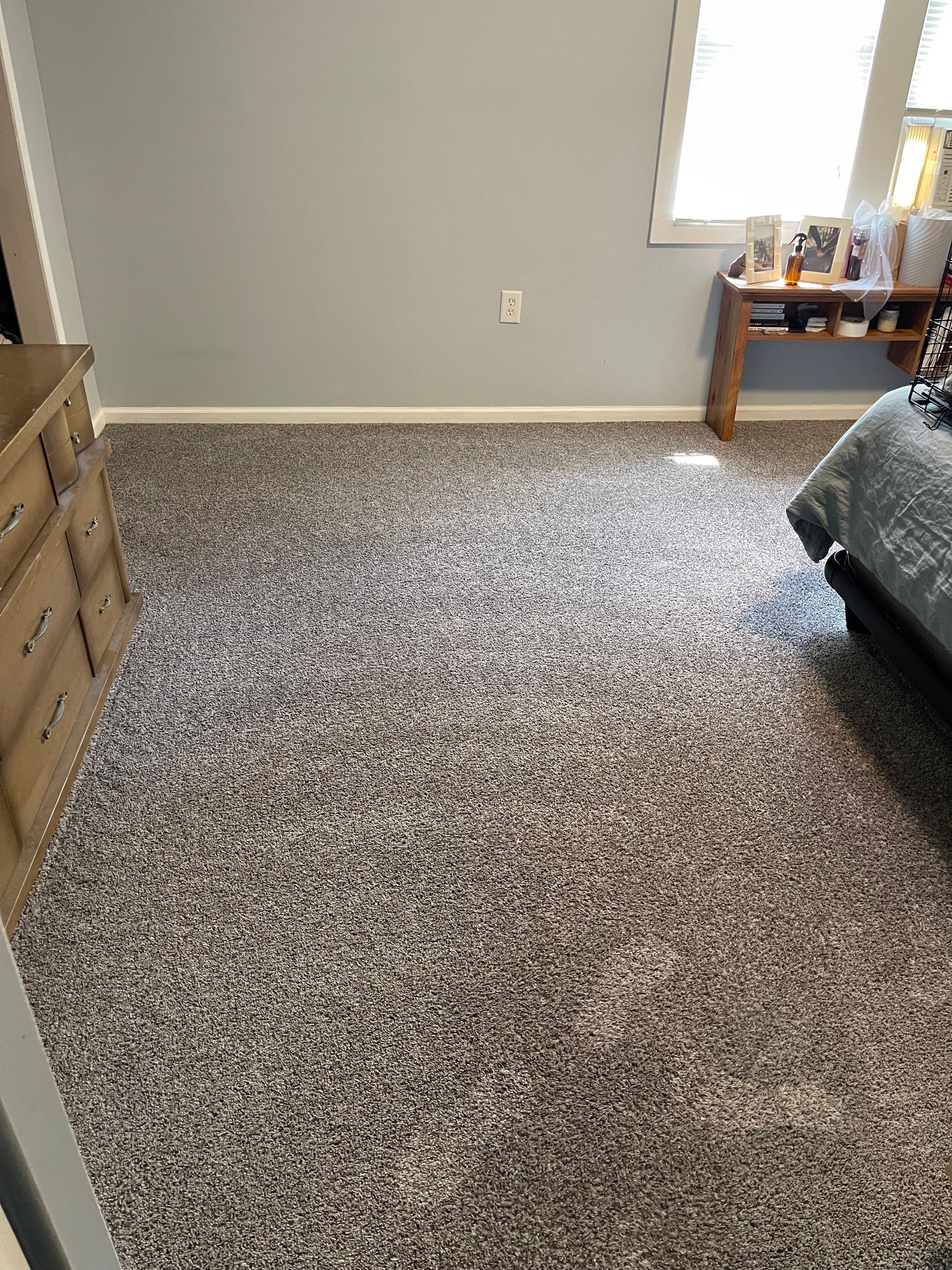 Bedroom with gray carpet, walls, dresser, bed, and window with sunlight.