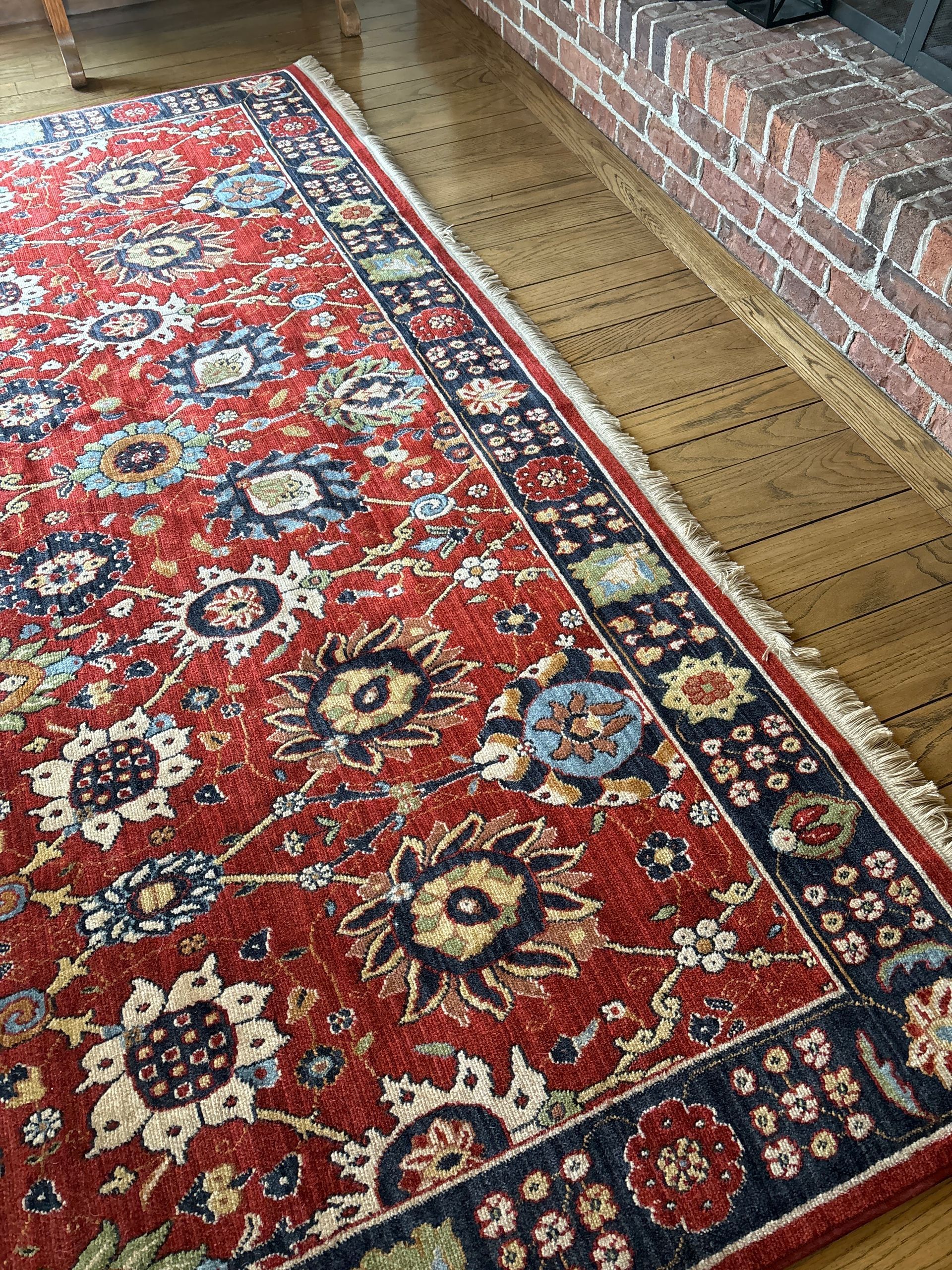 Red oriental rug with floral design and dark blue border on a wooden floor.