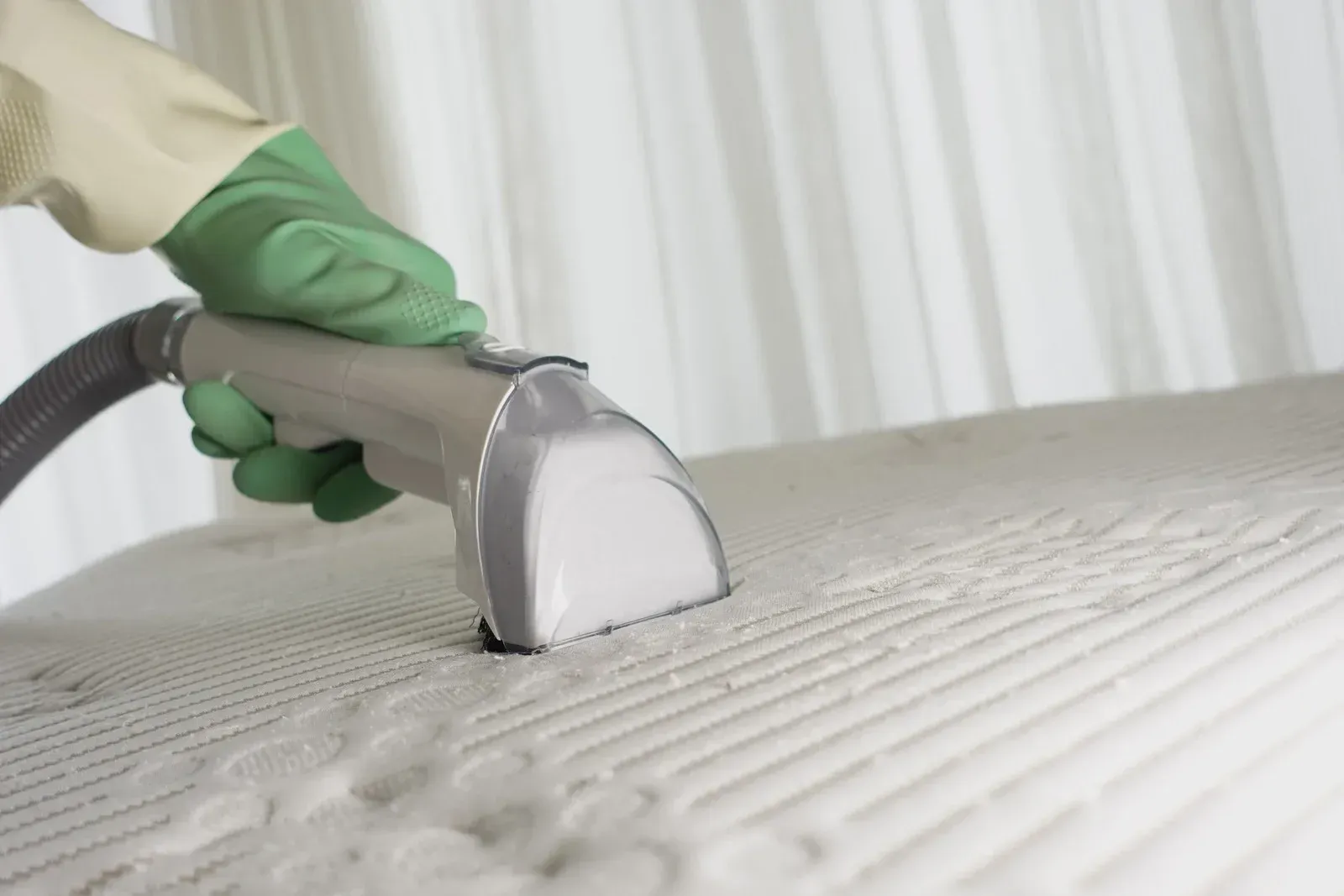 Person in green glove vacuums a white mattress.