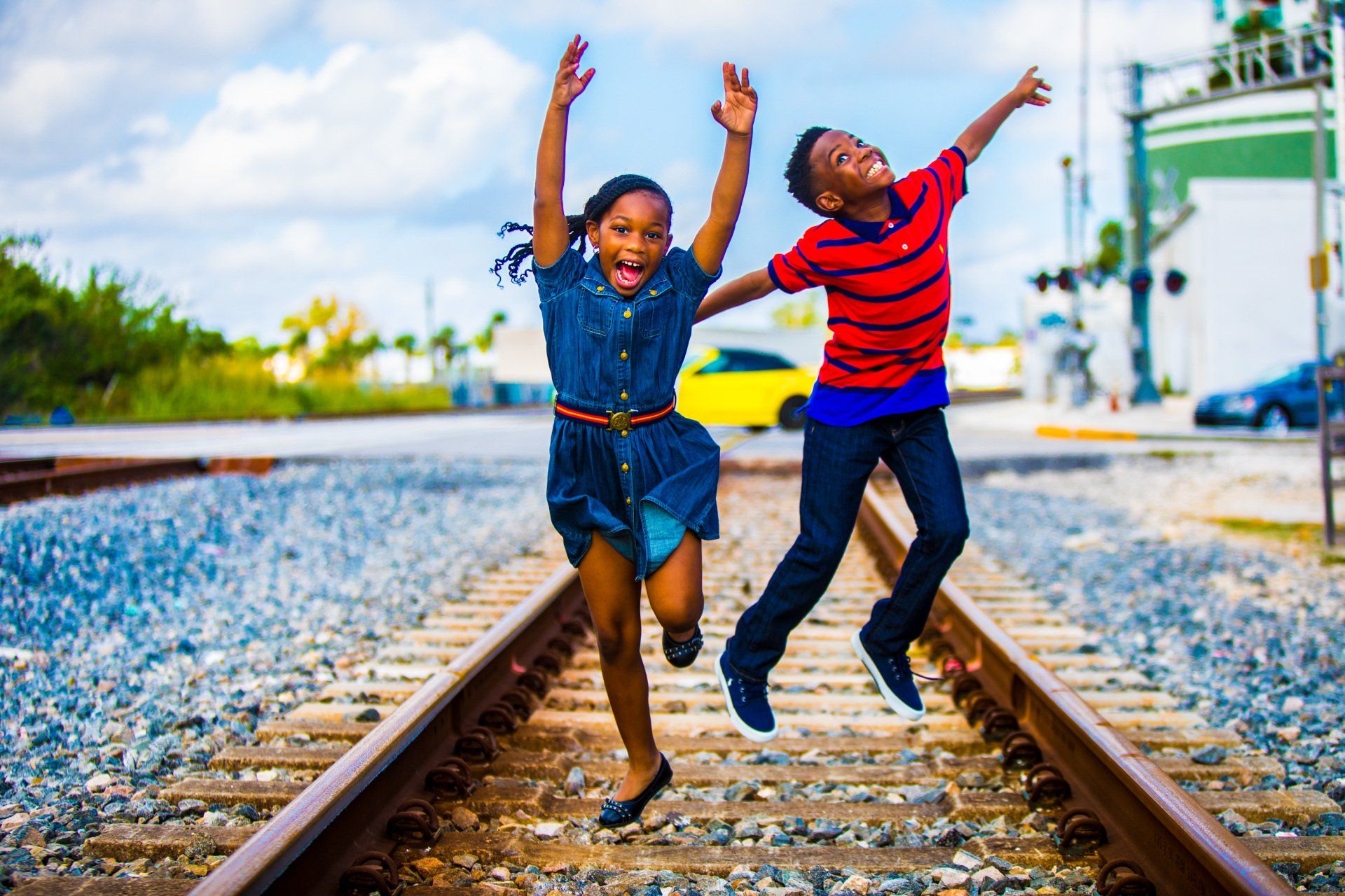 A boy and a girl are jumping in the air on train tracks.