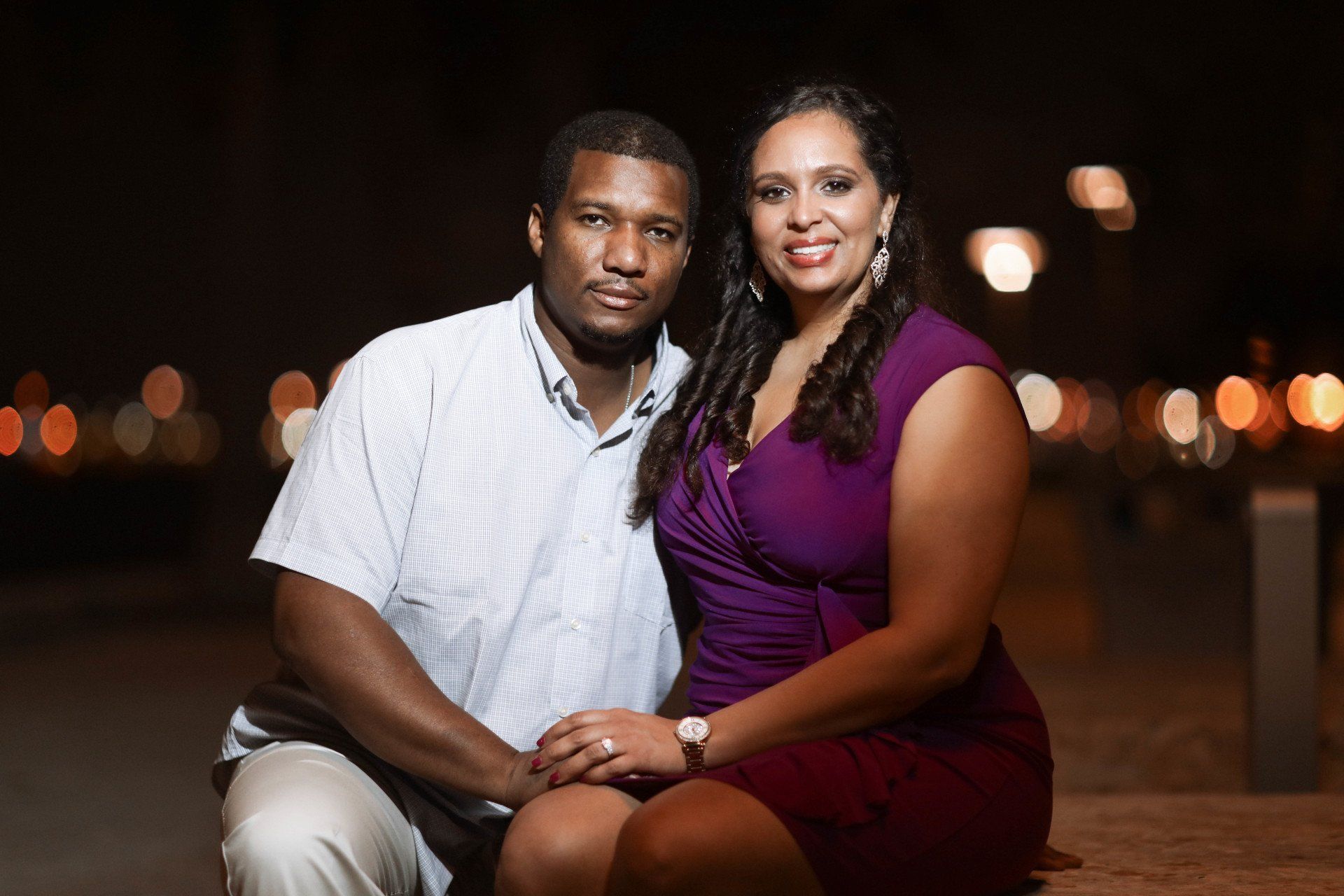 A man and a woman are posing for a picture at night . the woman is wearing a purple dress.