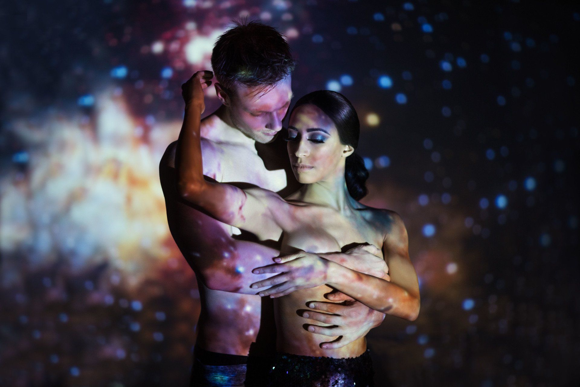 A man and a woman are hugging each other in front of a projection of a galaxy.