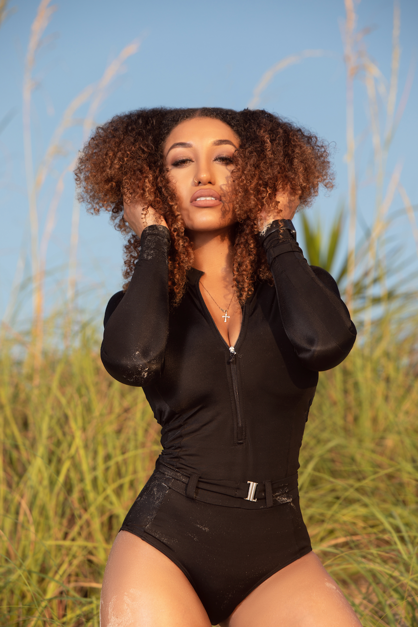 A woman in a black bodysuit is standing in a field of tall grass.