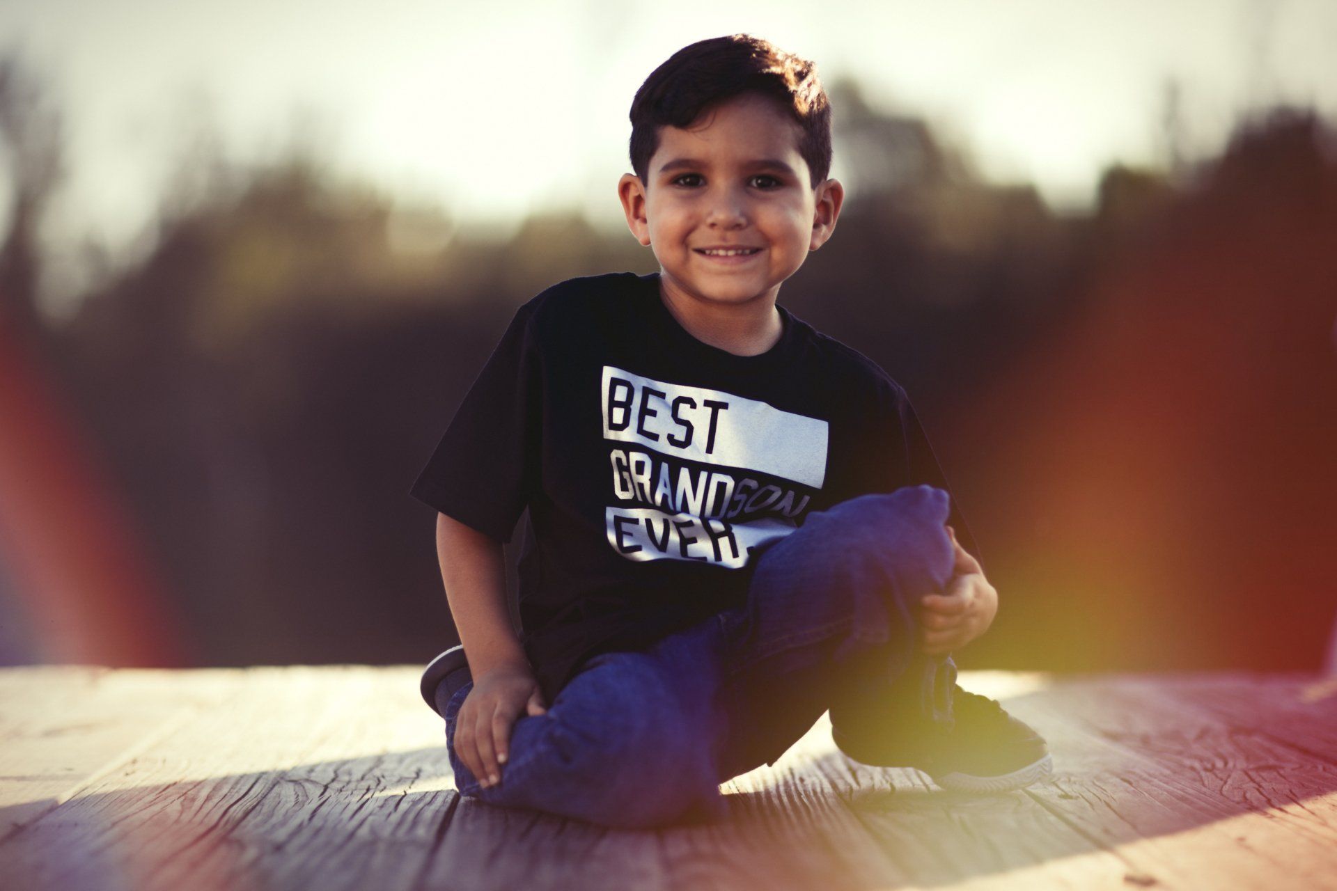 A young boy is sitting on the ground wearing a black shirt that says `` best brand ever ''.