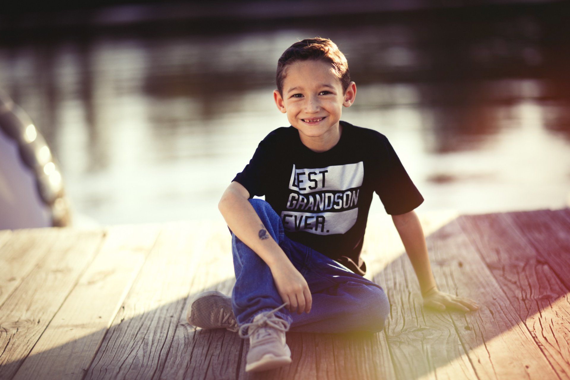 A young boy is sitting on a wooden dock.