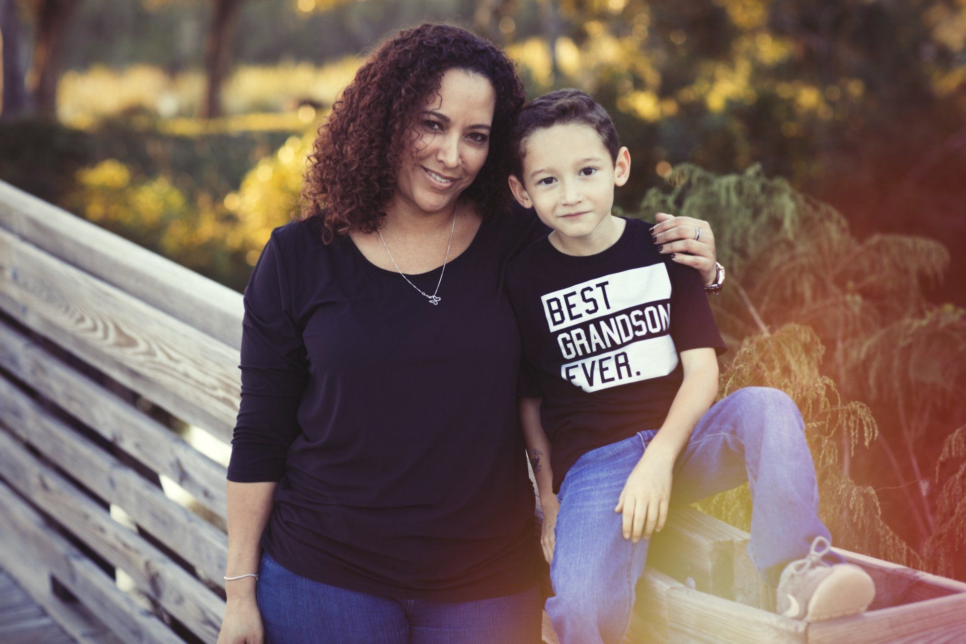 A woman and a boy are posing for a picture . the boy is wearing a shirt that says best grandson ever.