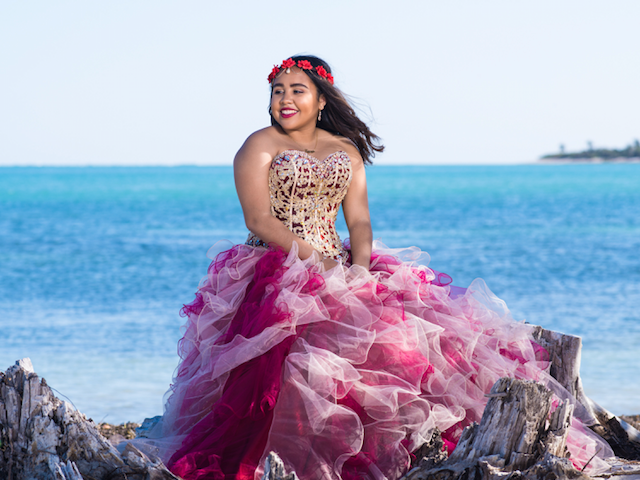 A woman in a pink and white dress is sitting on a rock near the ocean.