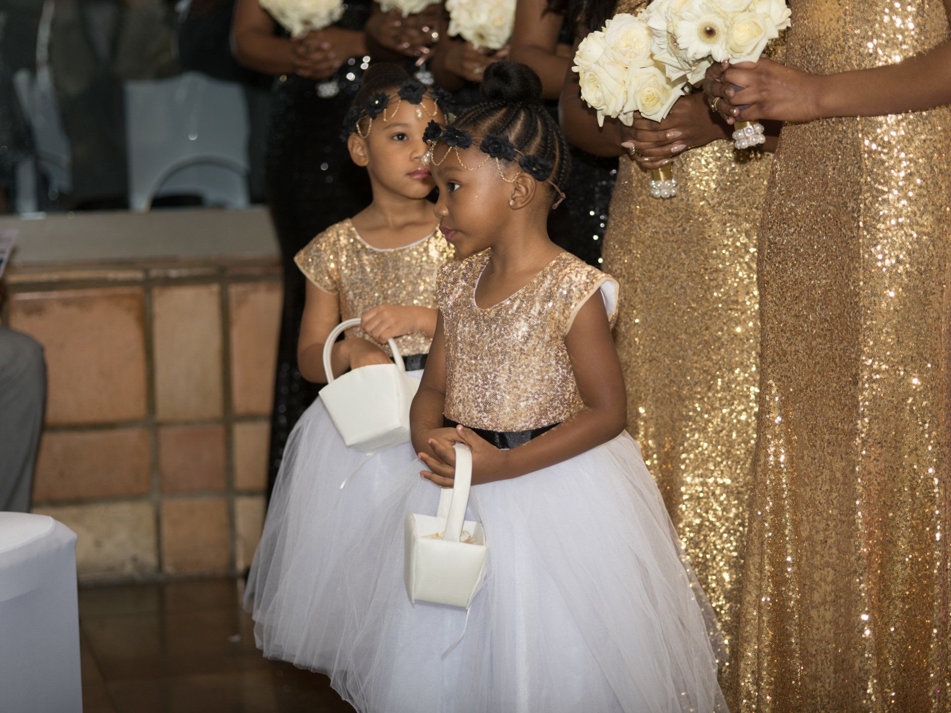 The flower girls are wearing gold and white dresses and holding baskets of flowers.