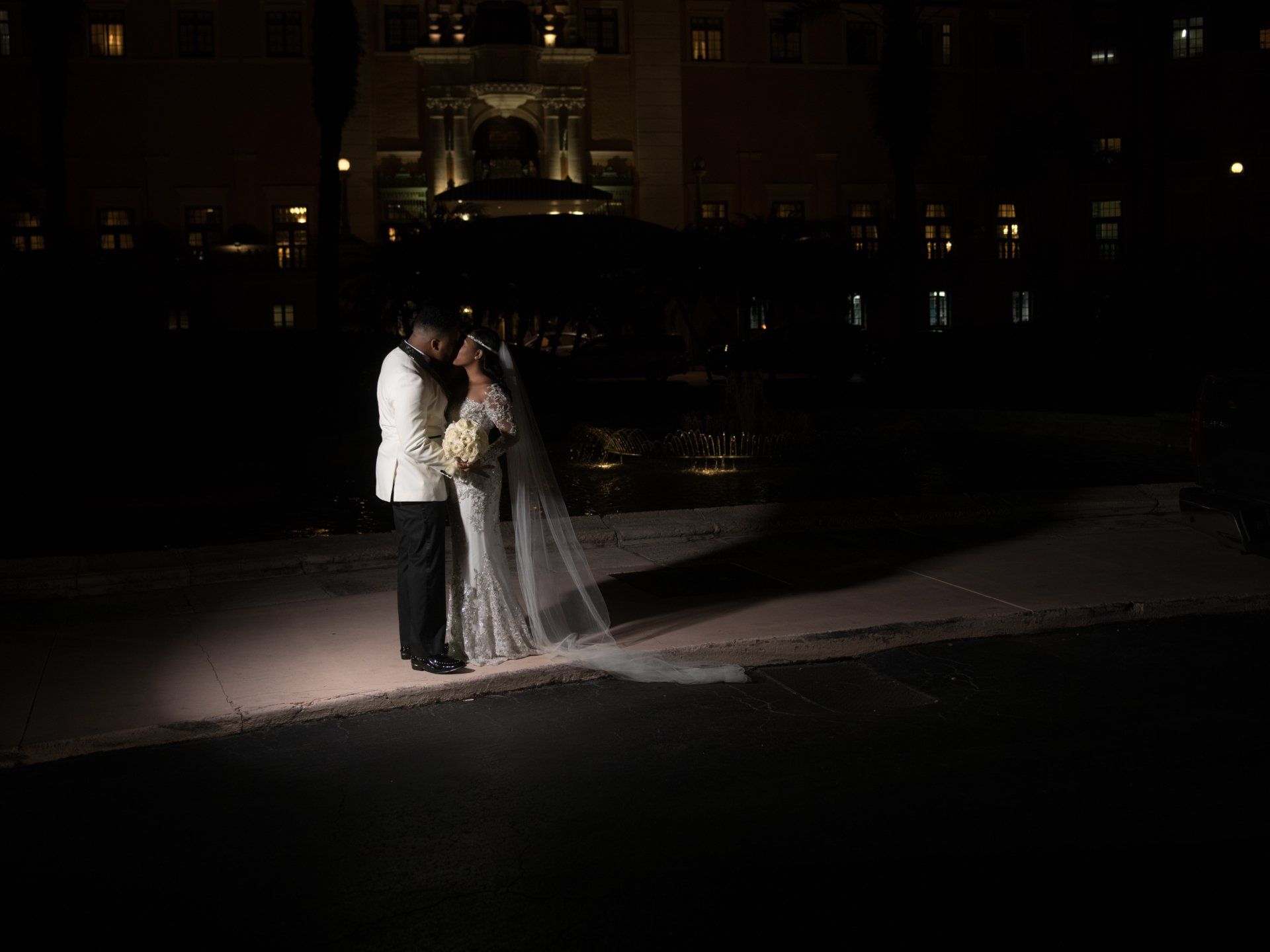 A bride and groom are standing in front of a building at night.