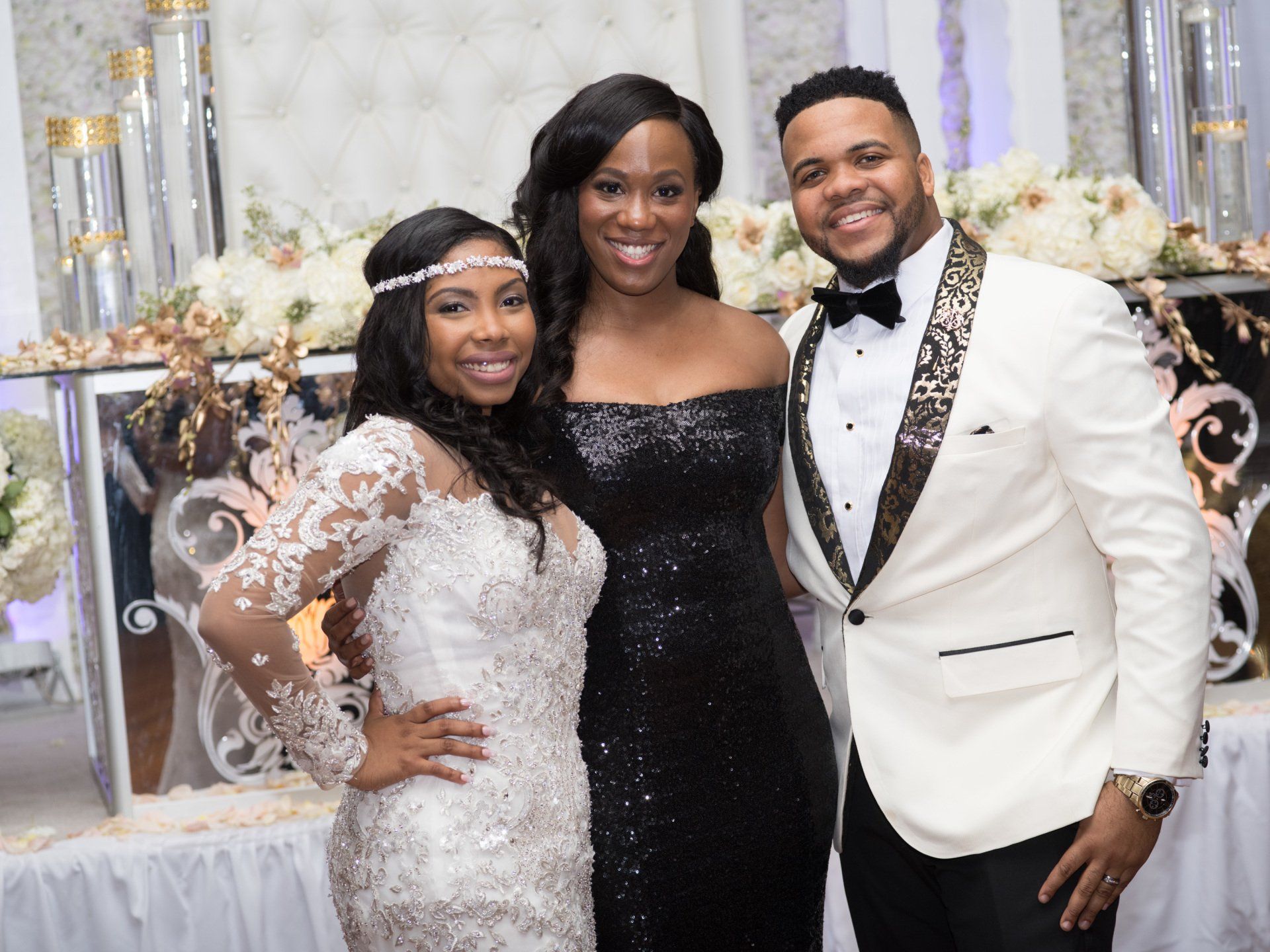 A bride and groom are posing for a picture with a woman in a black dress.
