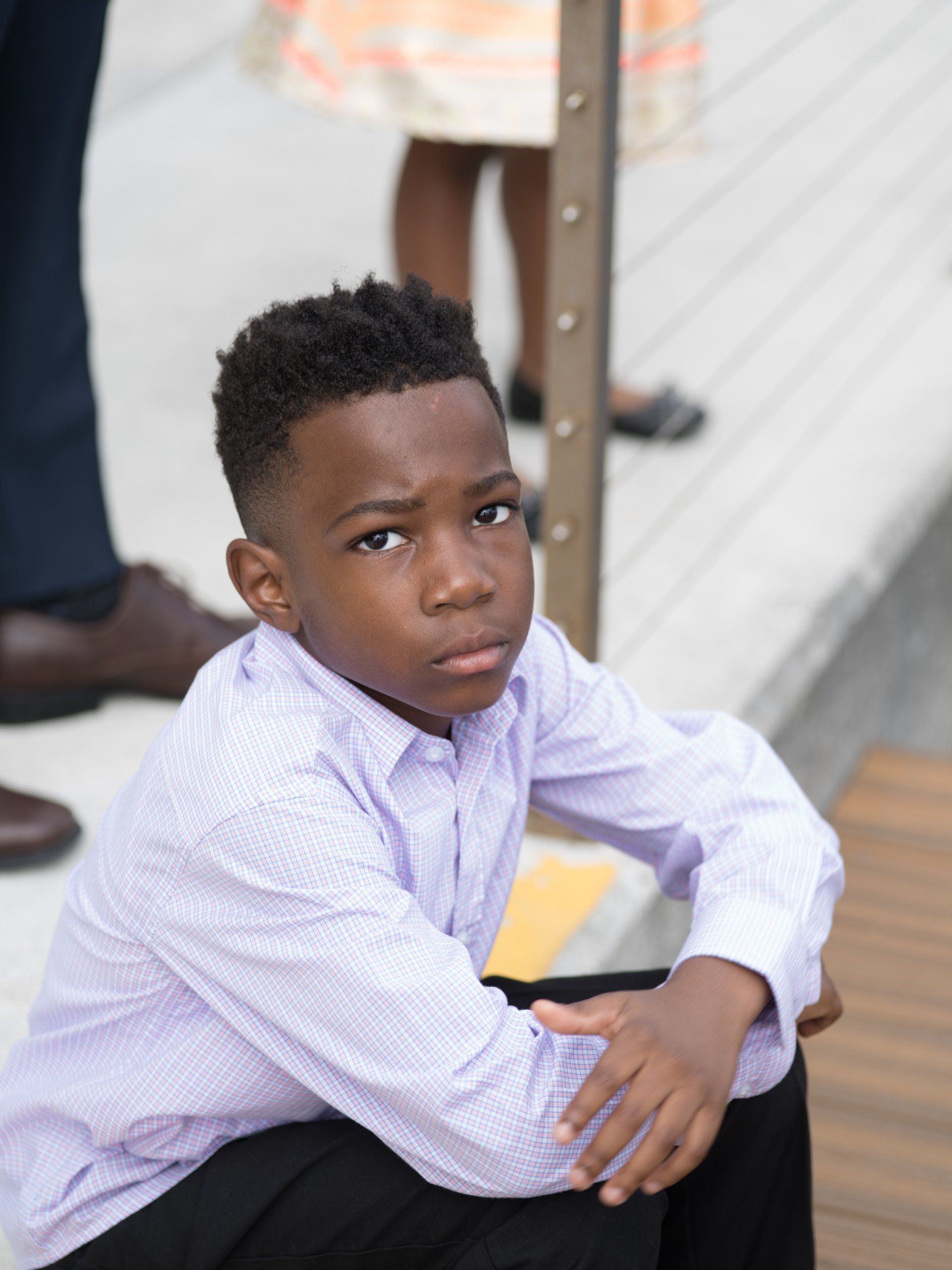 A young boy in a purple shirt and black pants is sitting on a wooden floor.