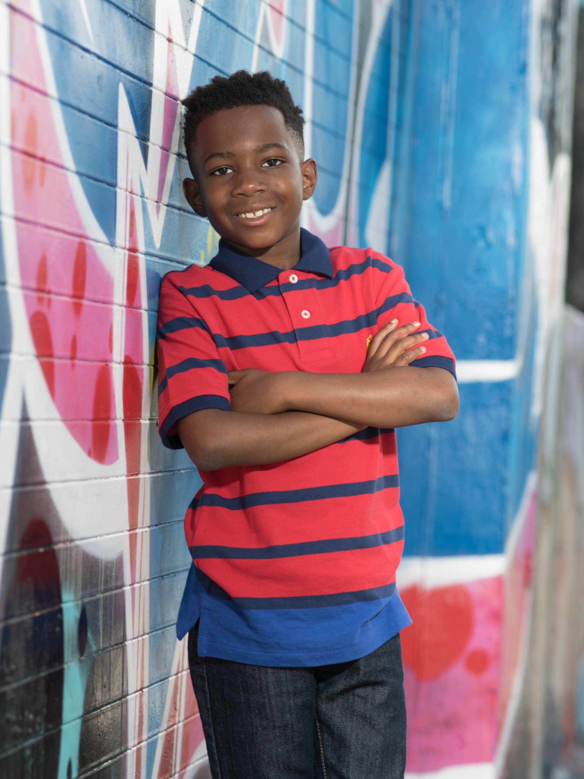 A young boy is leaning against a wall with his arms crossed.