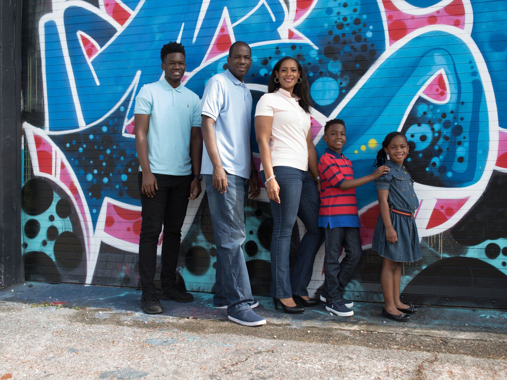 A family is posing for a picture in front of a graffiti wall.