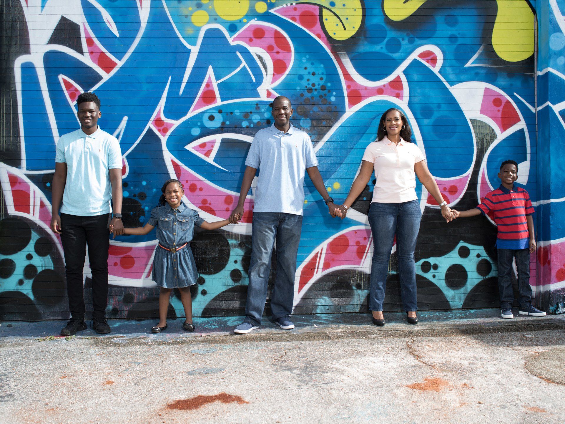 A family is standing in front of a graffiti wall holding hands.