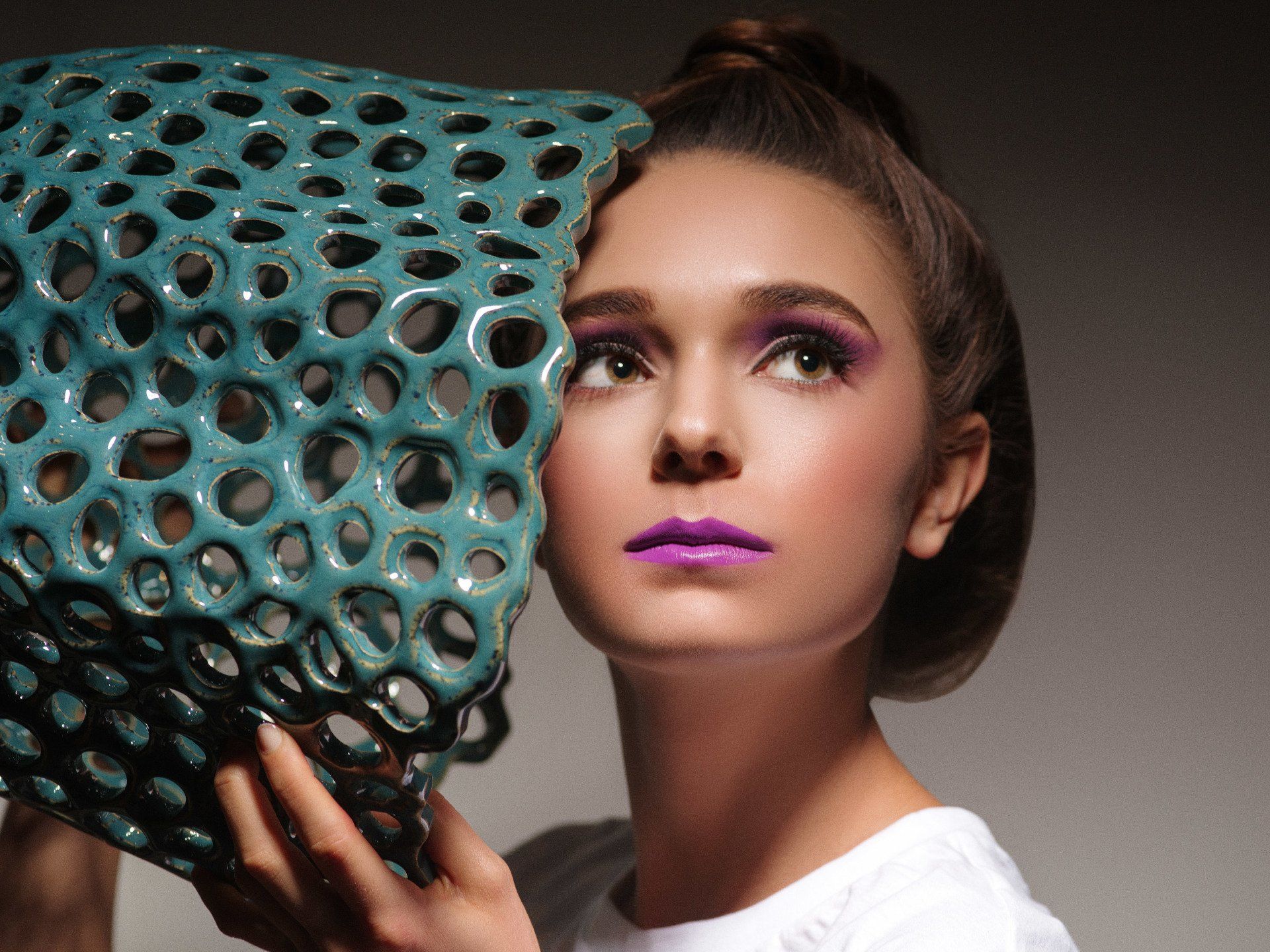 A woman with purple lips is holding a blue vase in front of her face