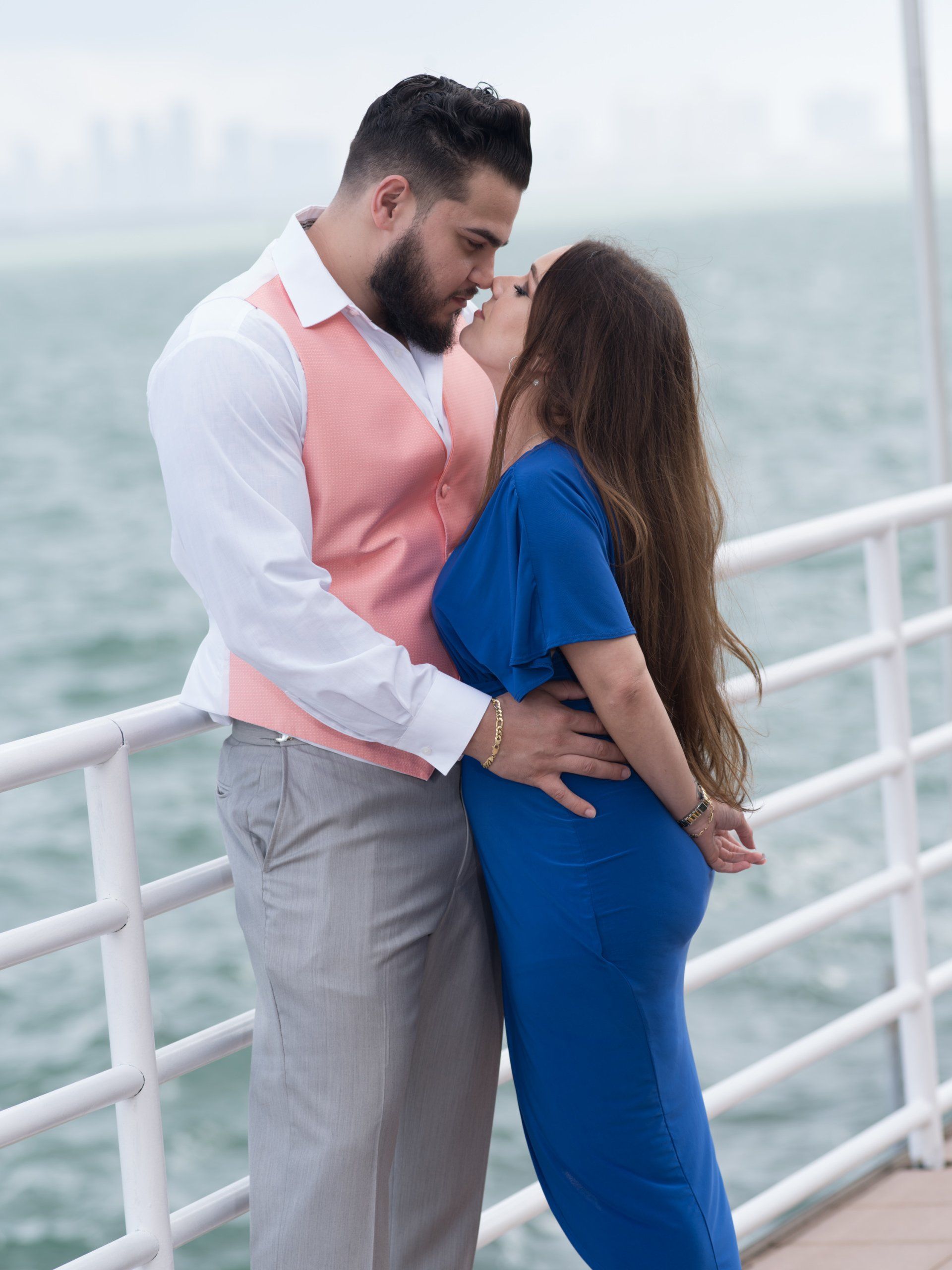 A man in a pink vest kisses a woman in a blue dress