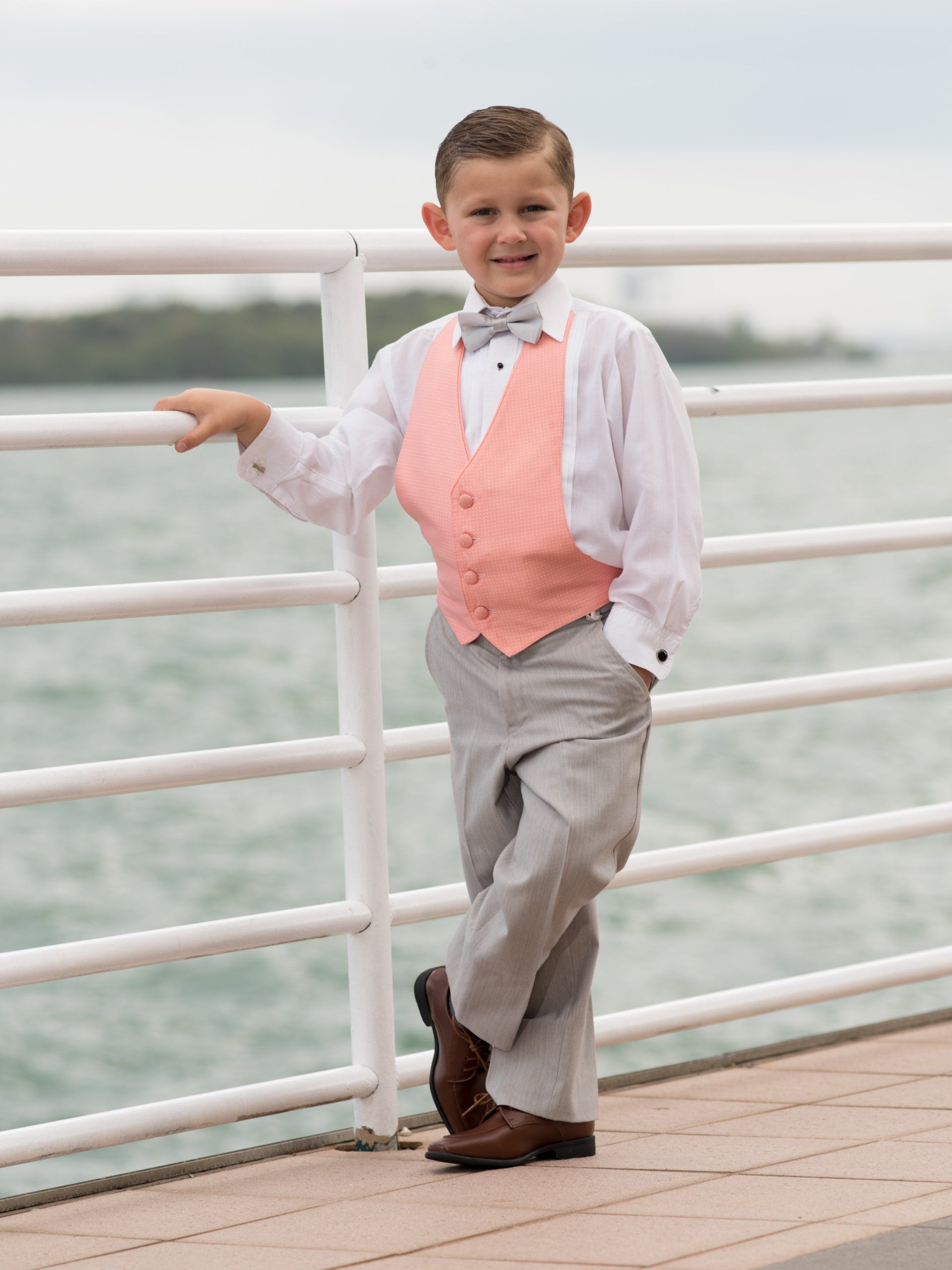 A young boy in a tuxedo is leaning against a railing.