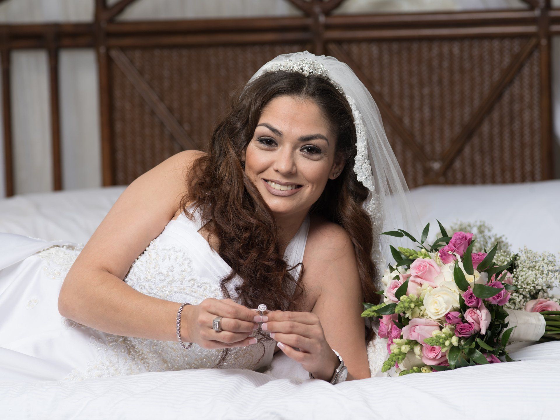 A bride is laying on a bed with a bouquet of flowers.