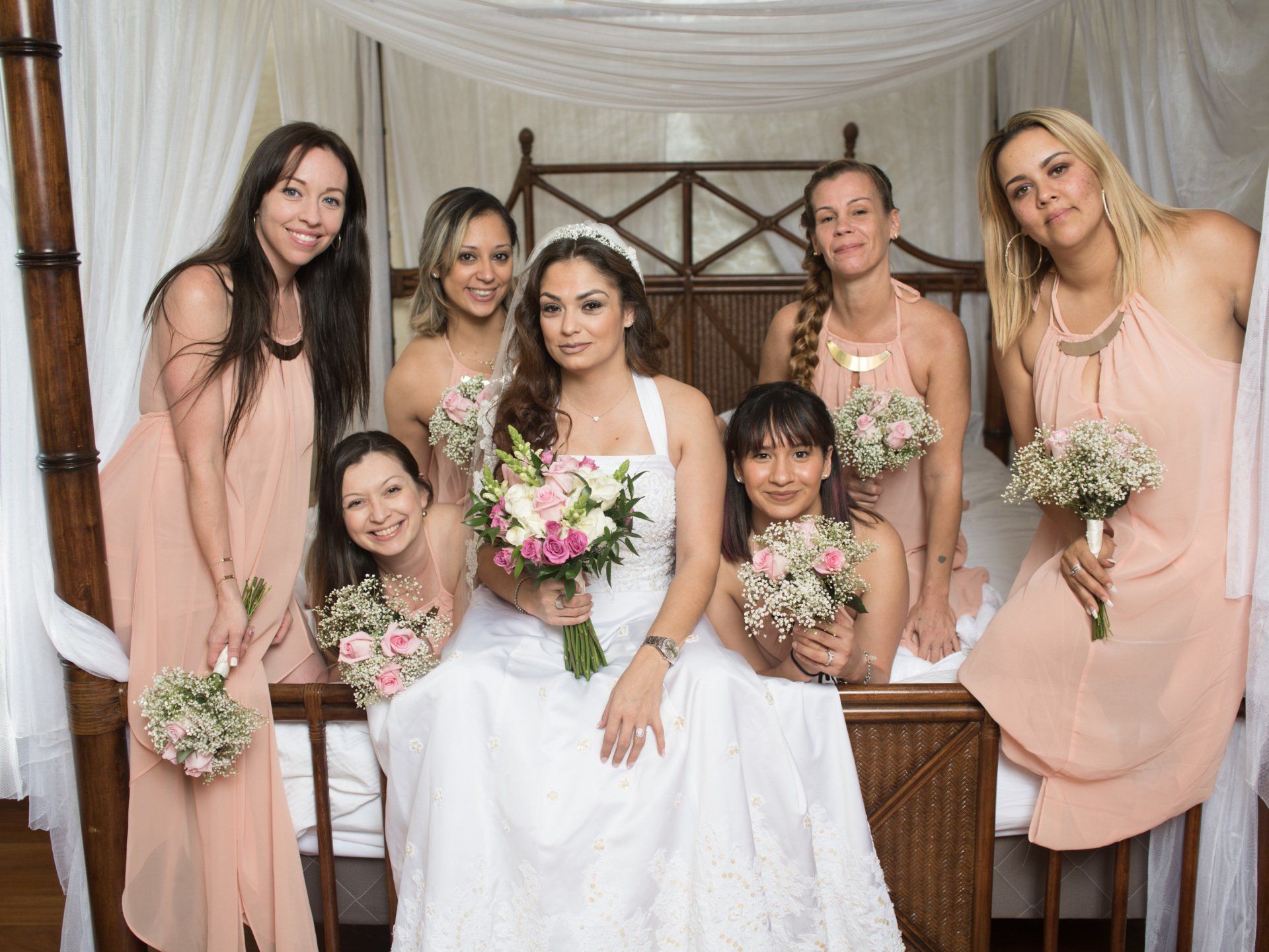 A bride and her bridesmaids are posing for a picture on a bed.
