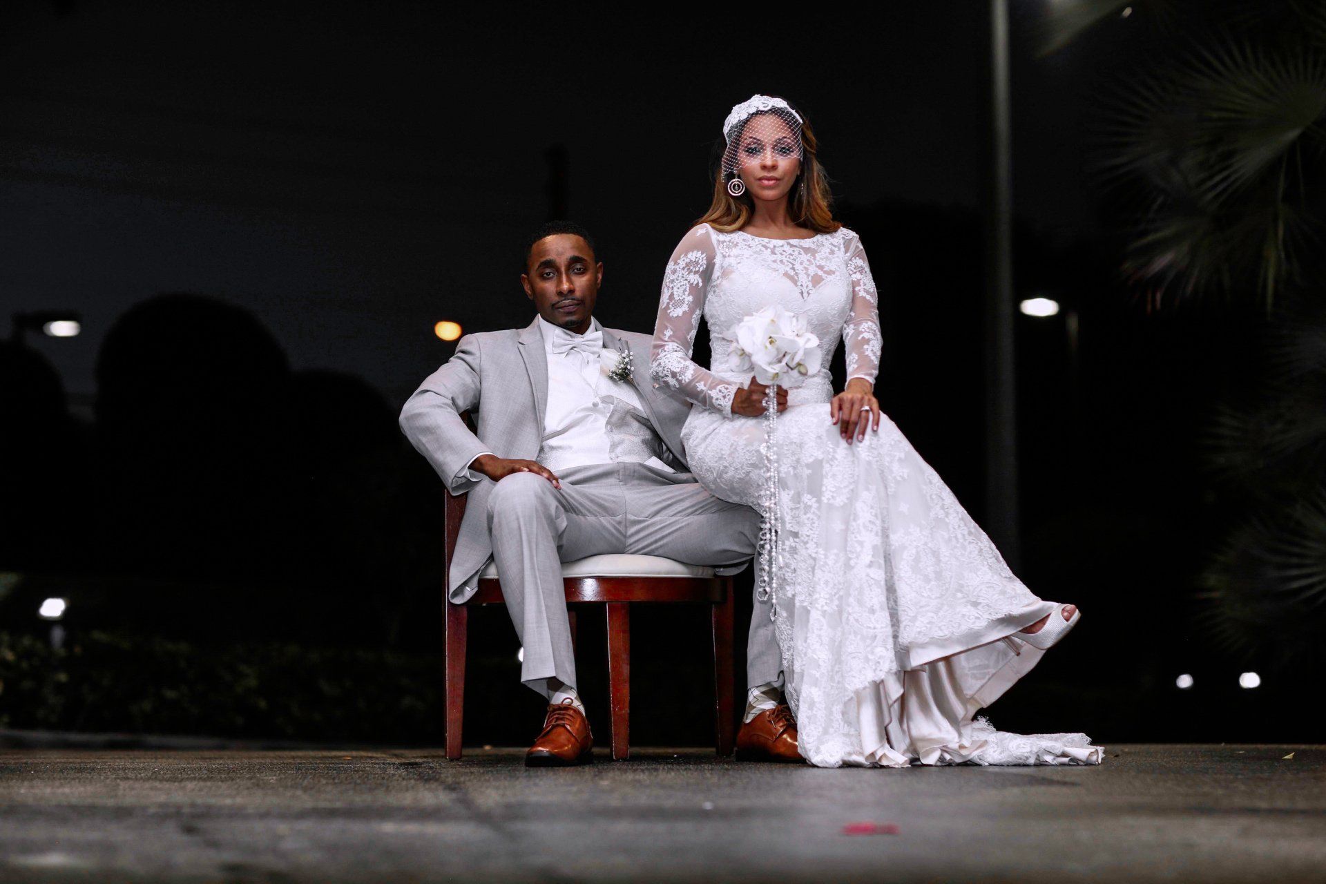 A bride and groom are posing for a picture while sitting in chairs.