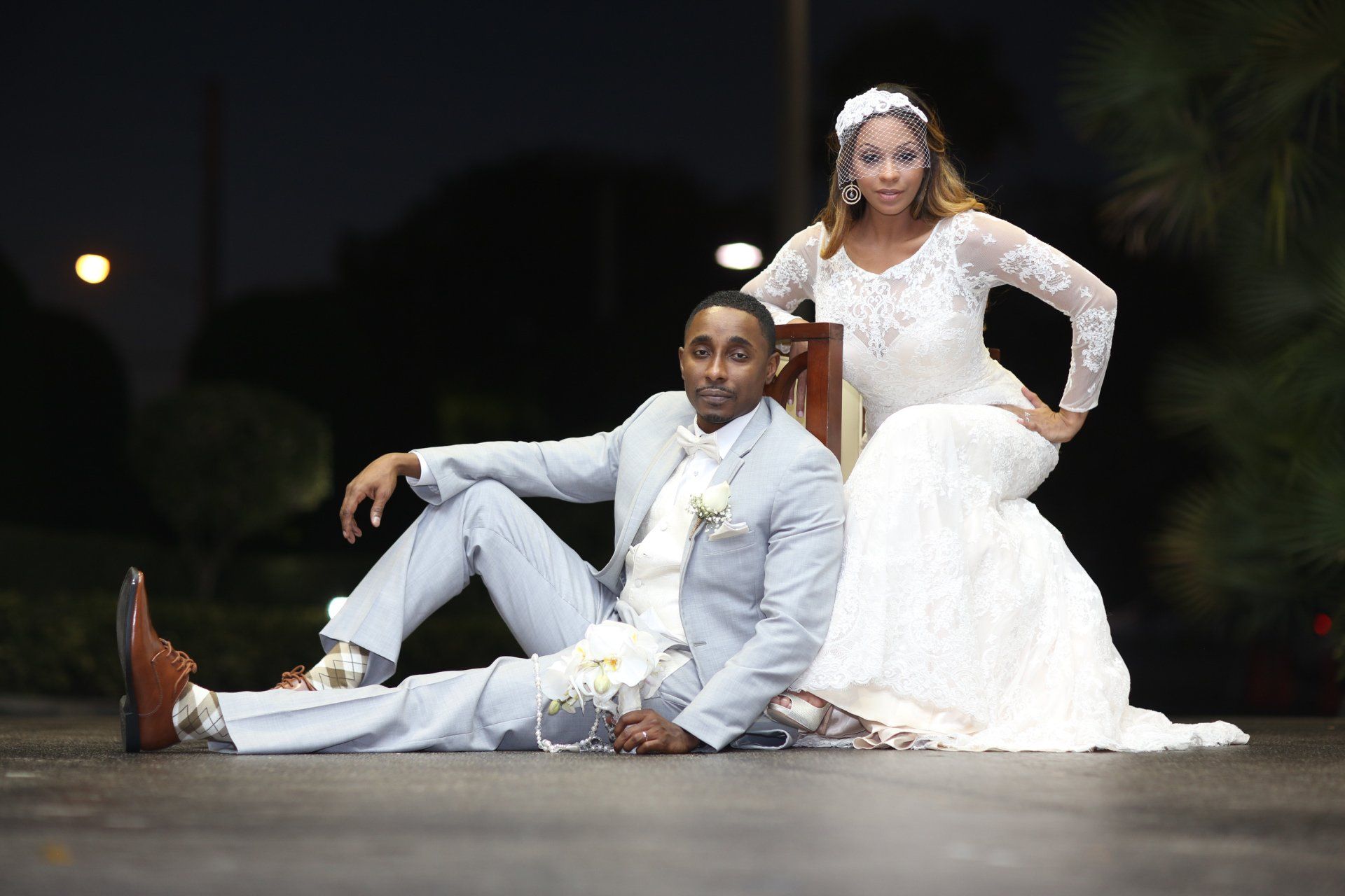 A bride and groom are posing for a picture while sitting on the ground.