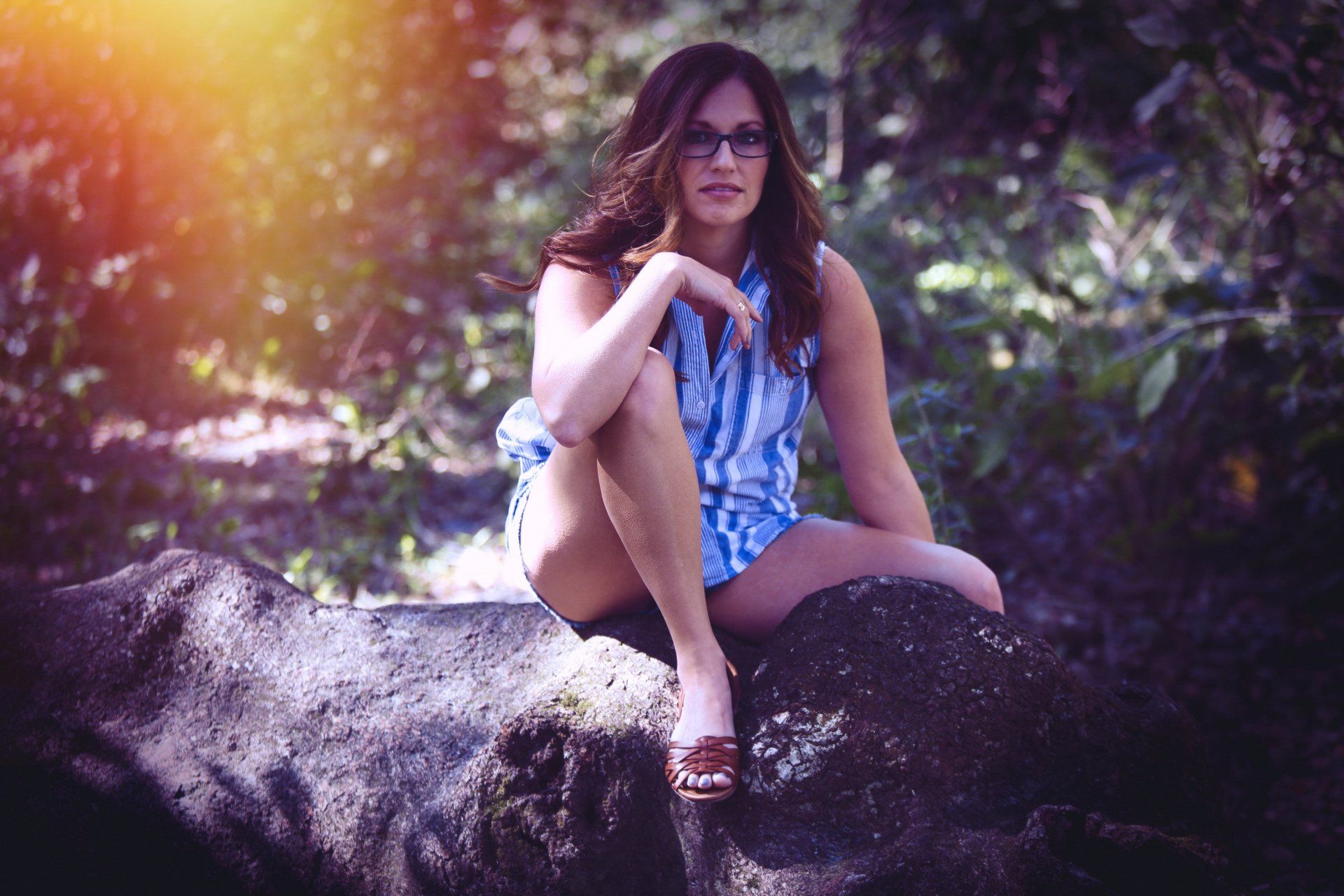 A woman is sitting on a rock in the woods.