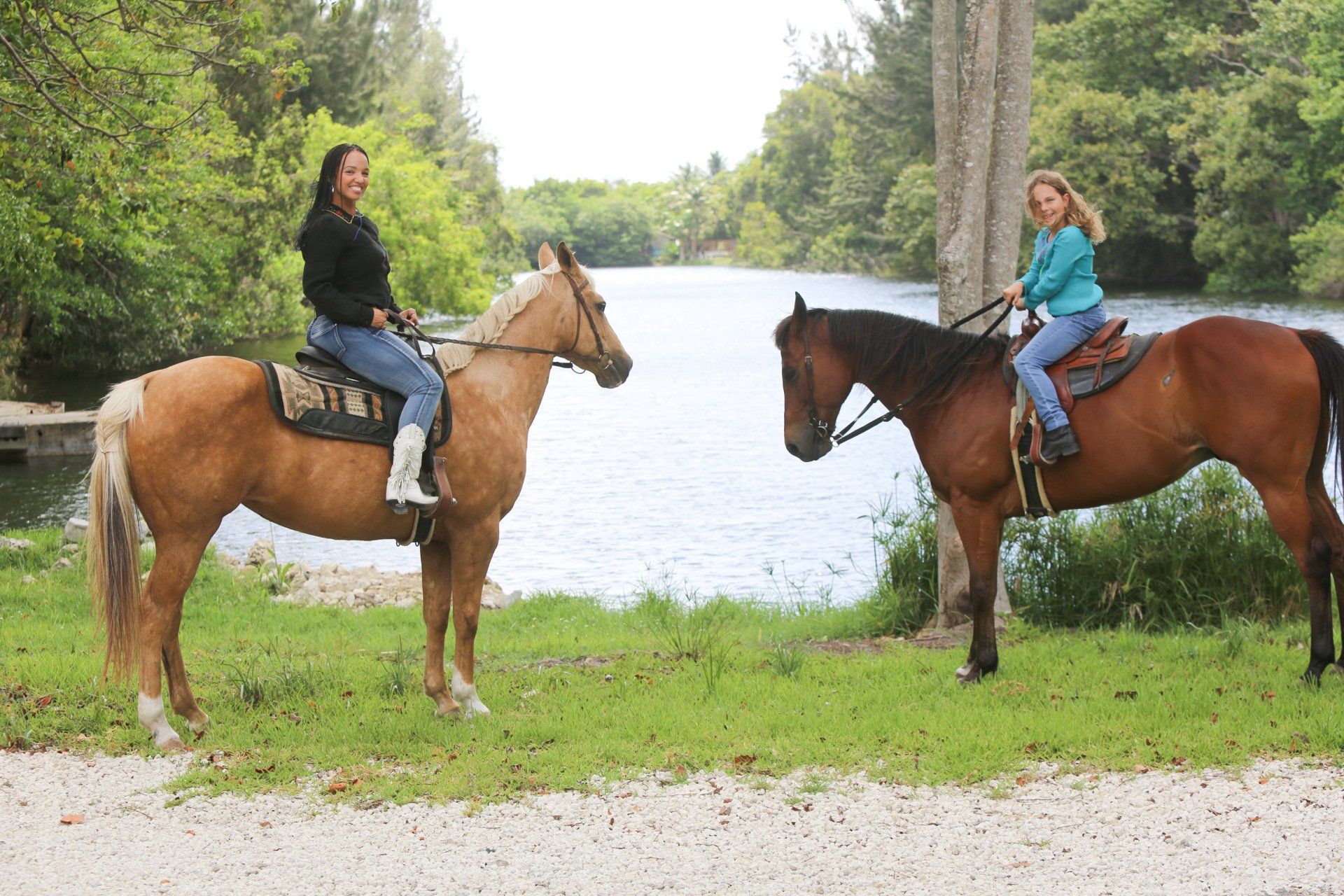 Two people are riding horses next to a river.