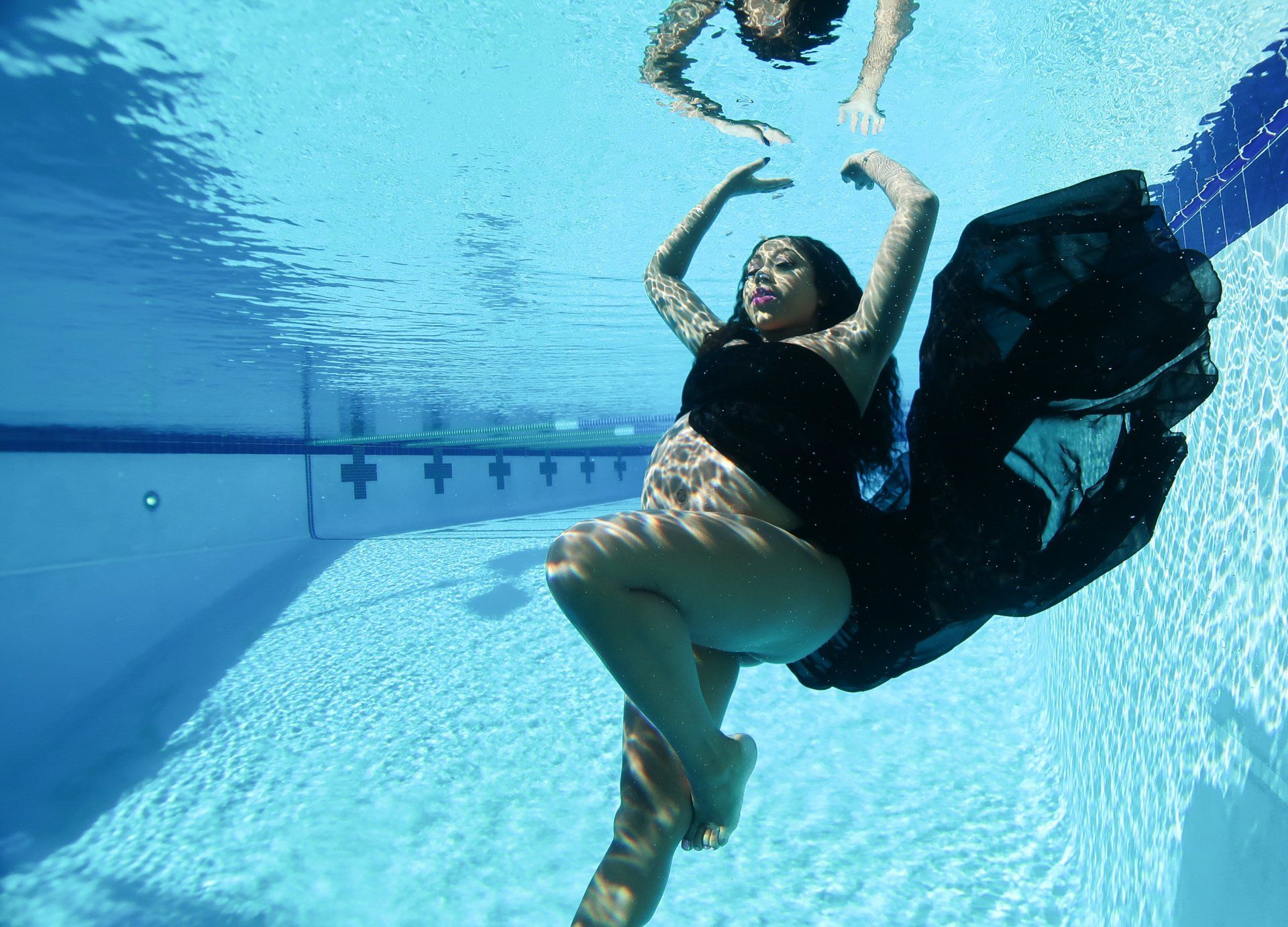 A pregnant woman is swimming underwater in a swimming pool.