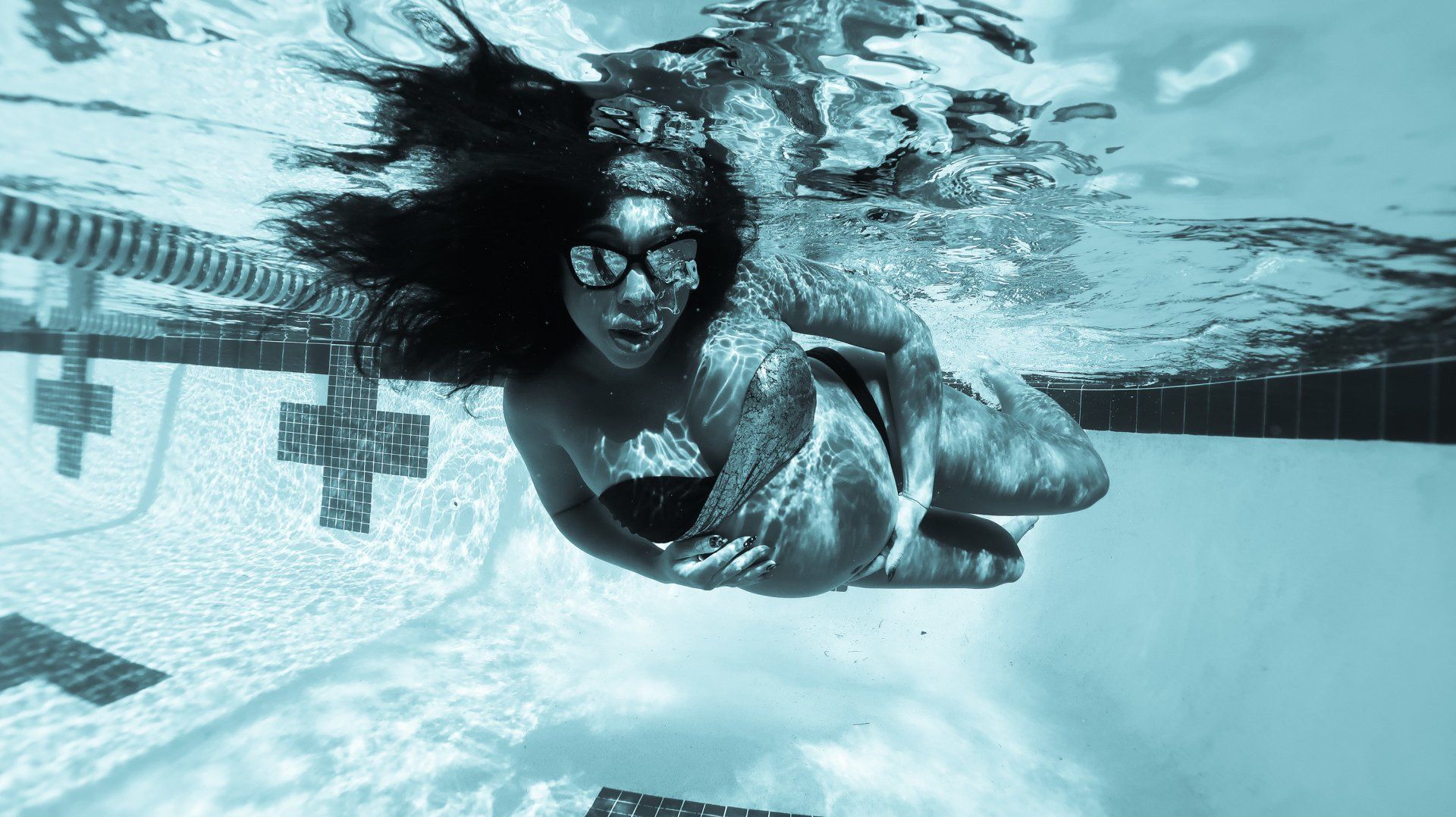 A woman is swimming underwater in a swimming pool.