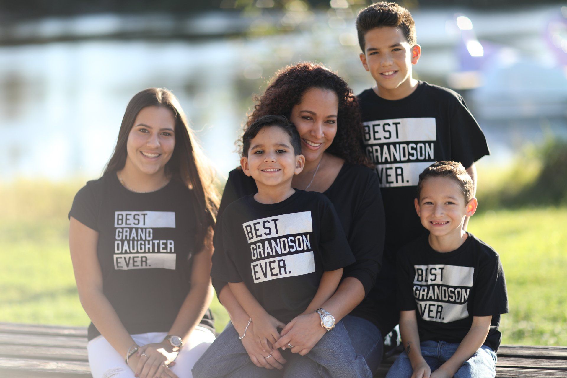 A family is posing for a picture while wearing matching shirts that say best grandson ever.