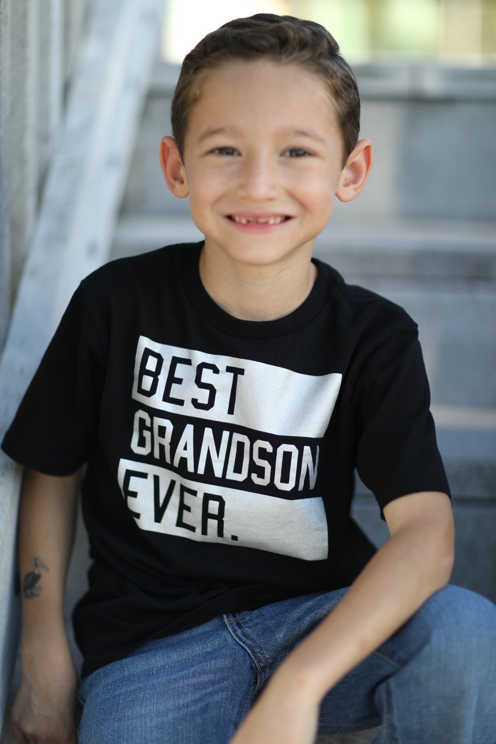 A young boy wearing a black shirt that says best grandson ever