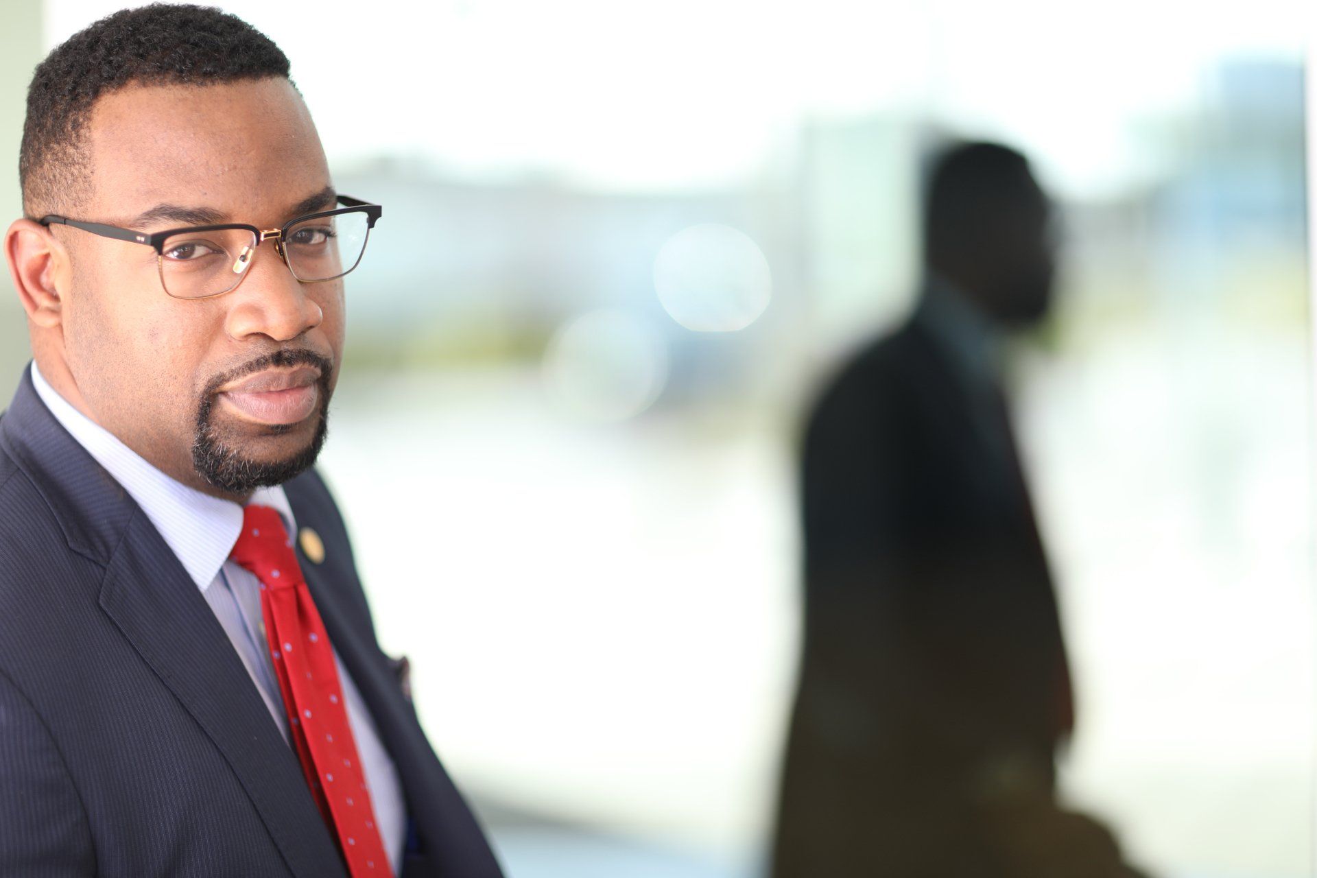 A man in a suit and tie is standing in front of a window.