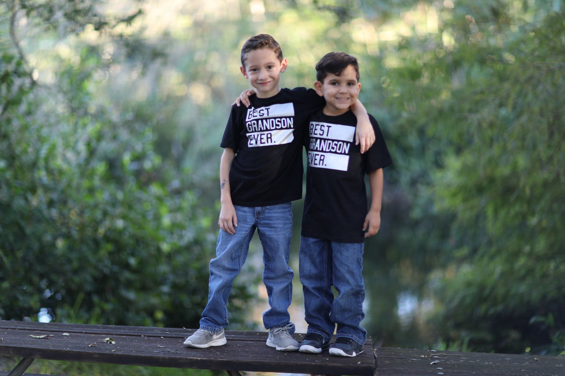 Two young boys are standing next to each other on a picnic table.