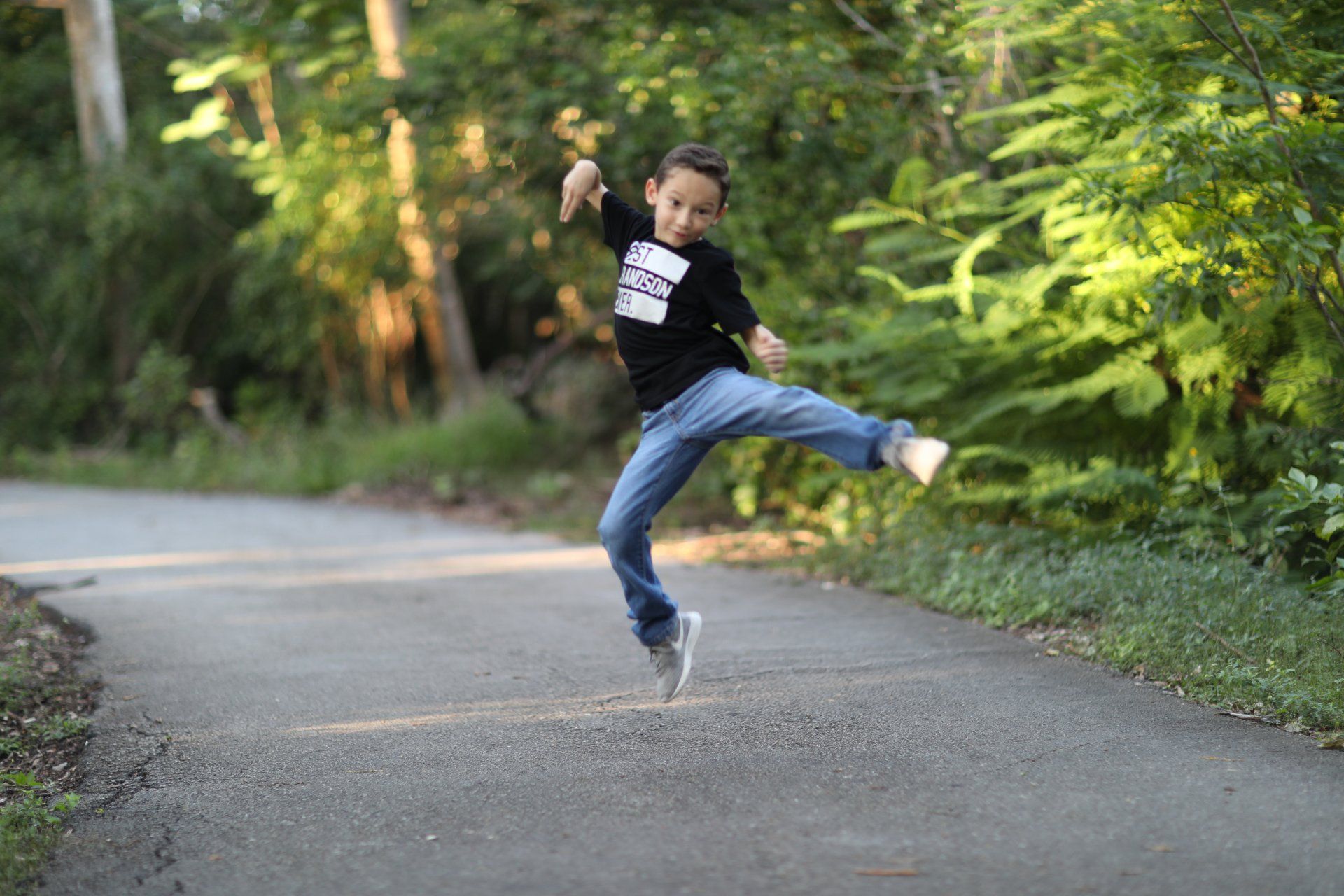 A young boy is jumping in the air on a road.
