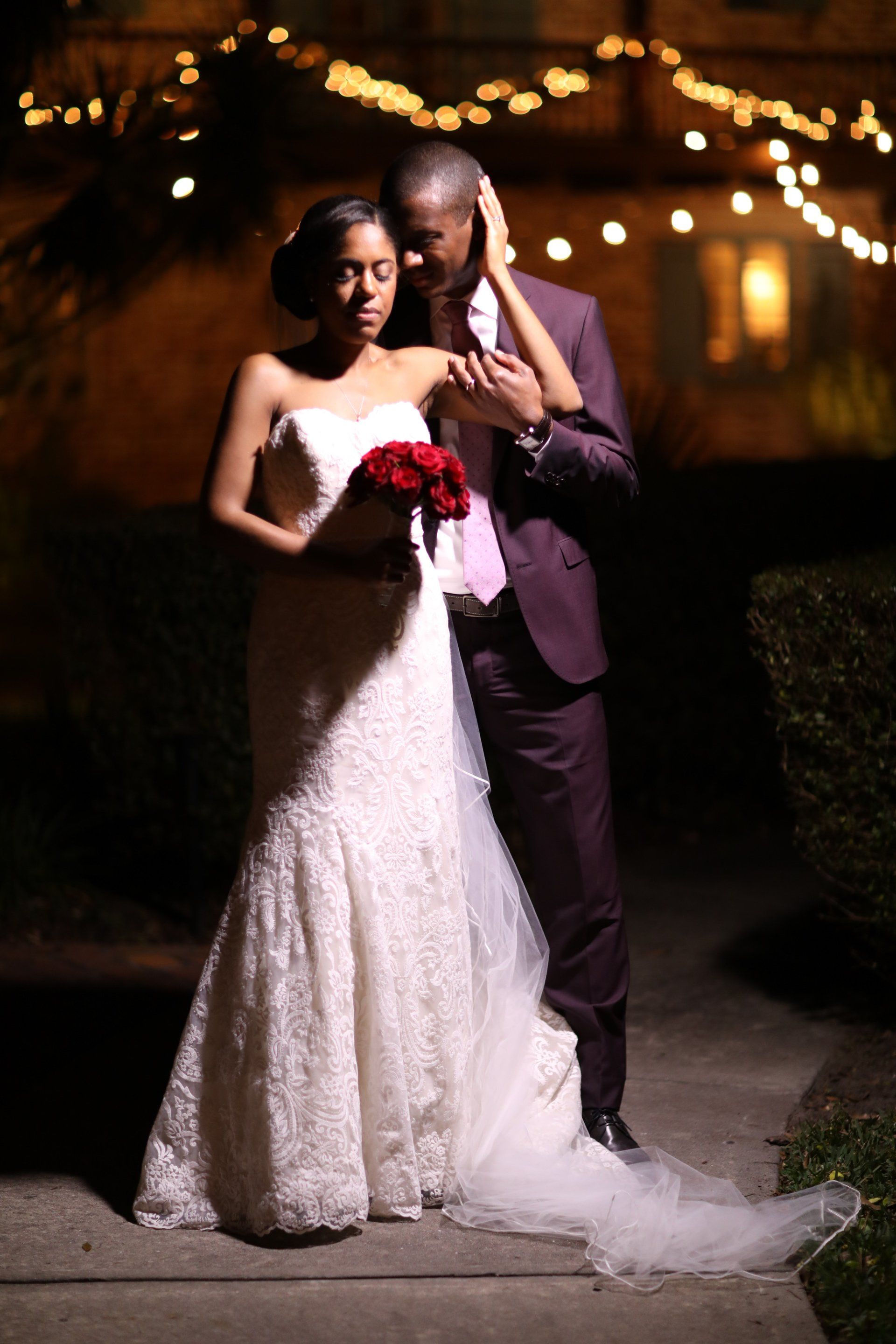A bride and groom are standing next to each other on a sidewalk at night.