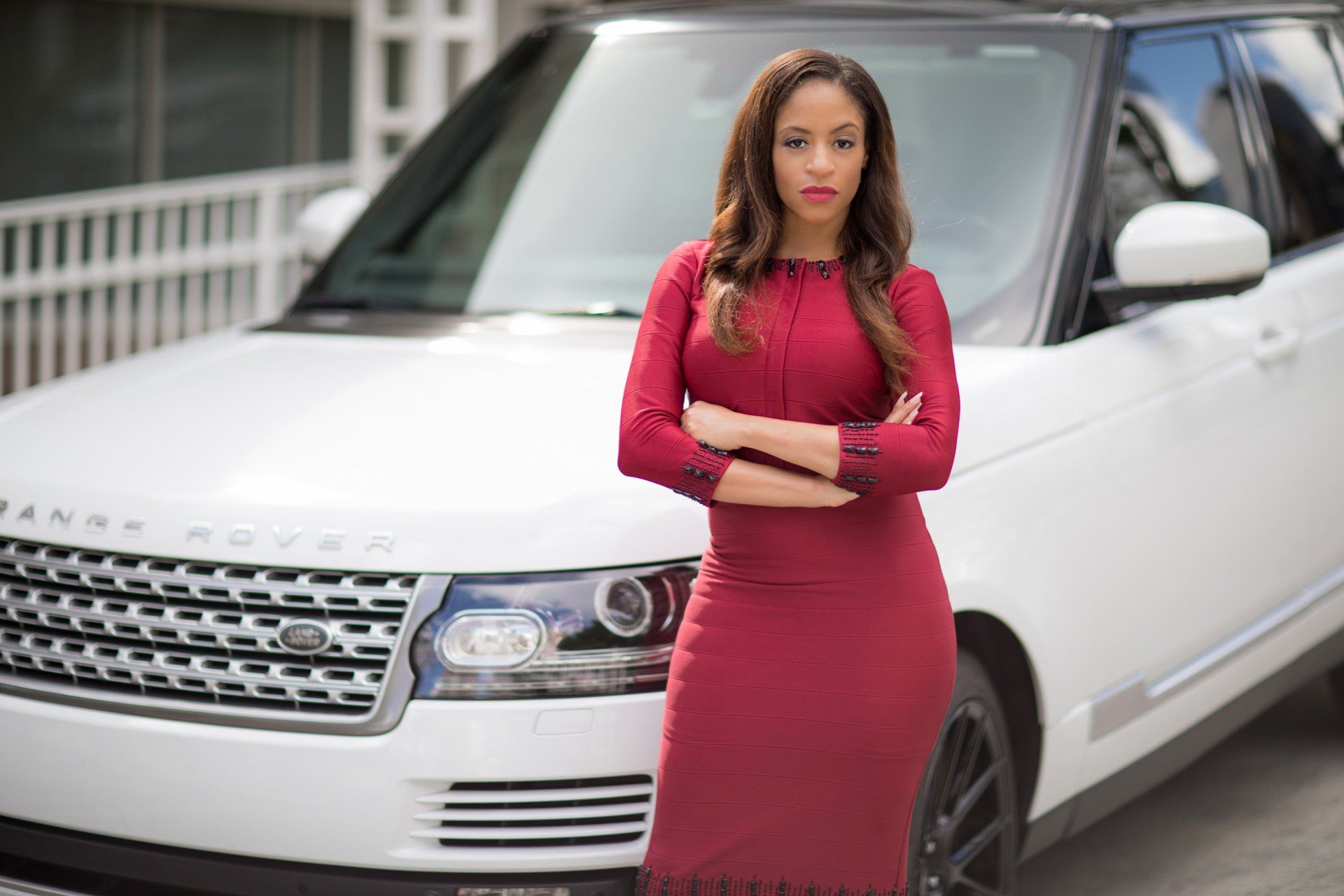 A woman in a red dress is standing in front of a white range rover.