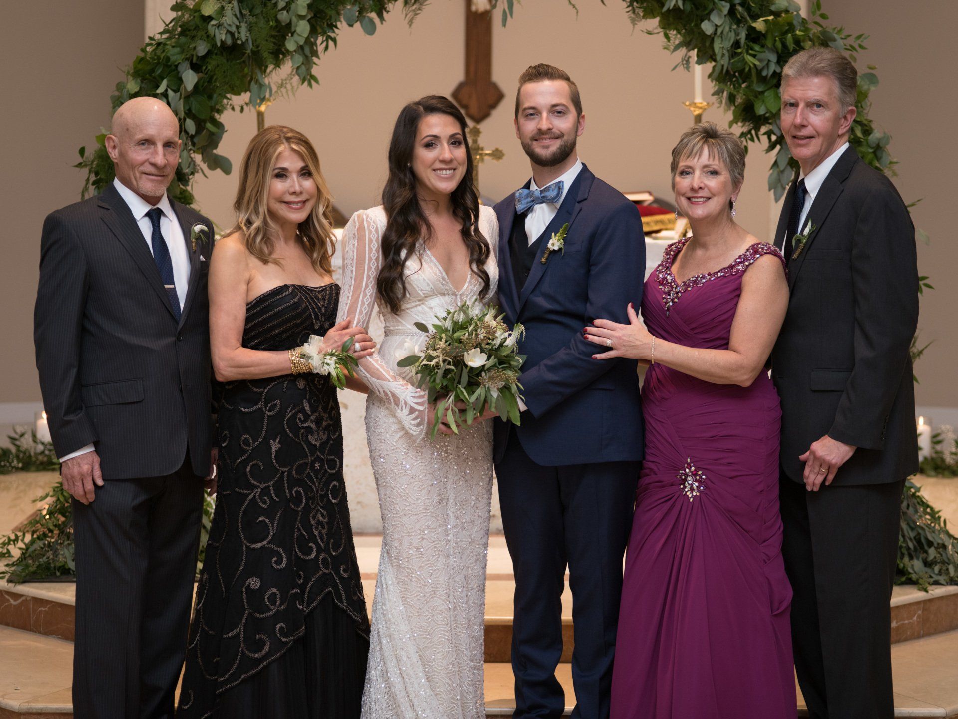 The bride and groom are posing for a picture with their parents.