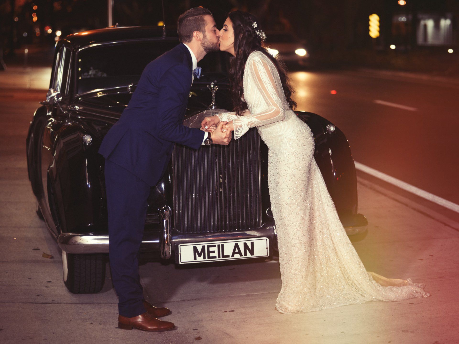 A bride and groom kissing in front of a rolls royce