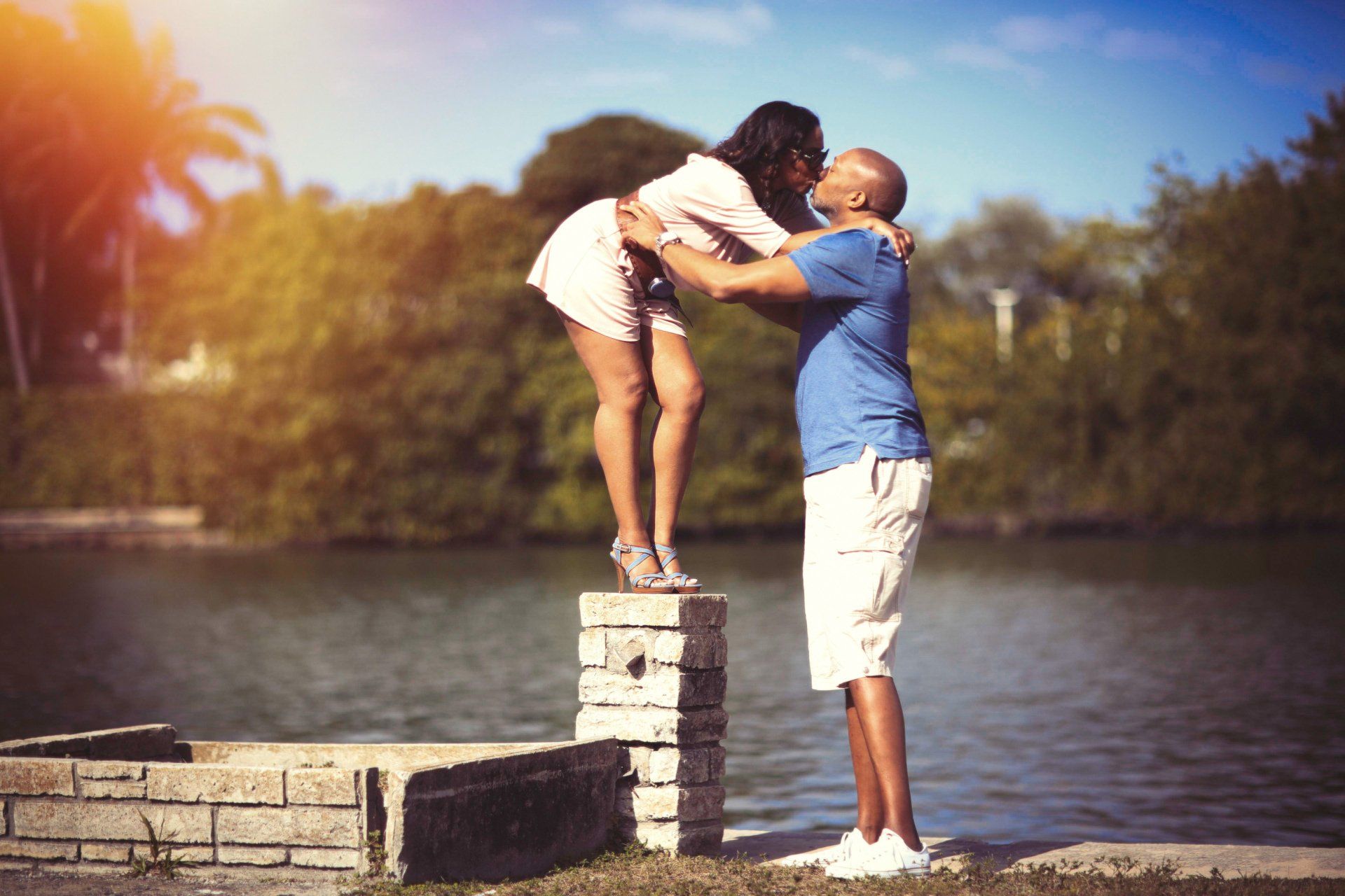 A man is kissing a woman while standing on a brick wall next to a body of water.