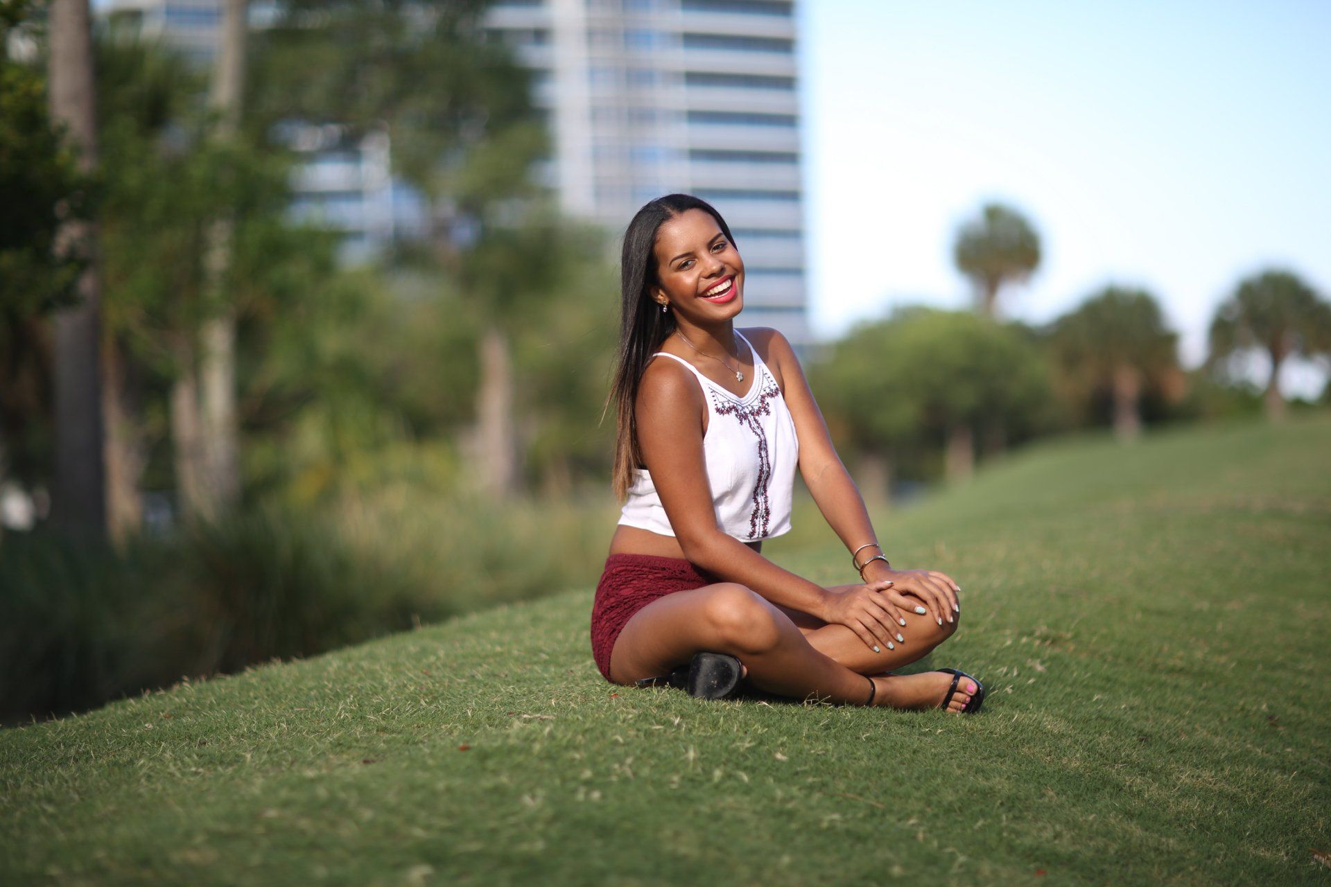 A woman is sitting on the grass with her legs crossed and smiling.