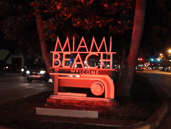 A miami beach welcome sign is lit up at night