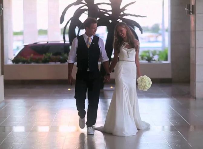 A bride and groom are walking down a hallway holding hands.