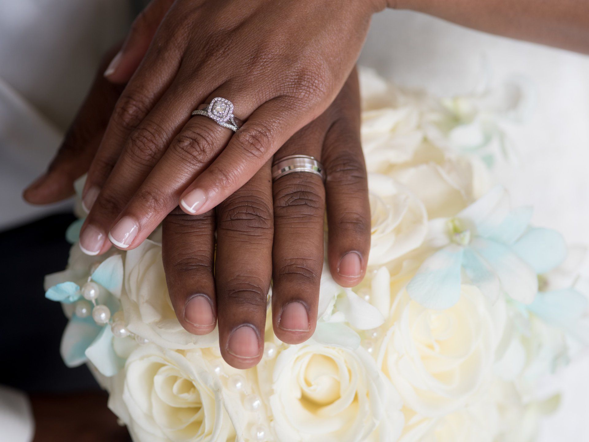 A bride and groom are putting their wedding rings on a bouquet of flowers.