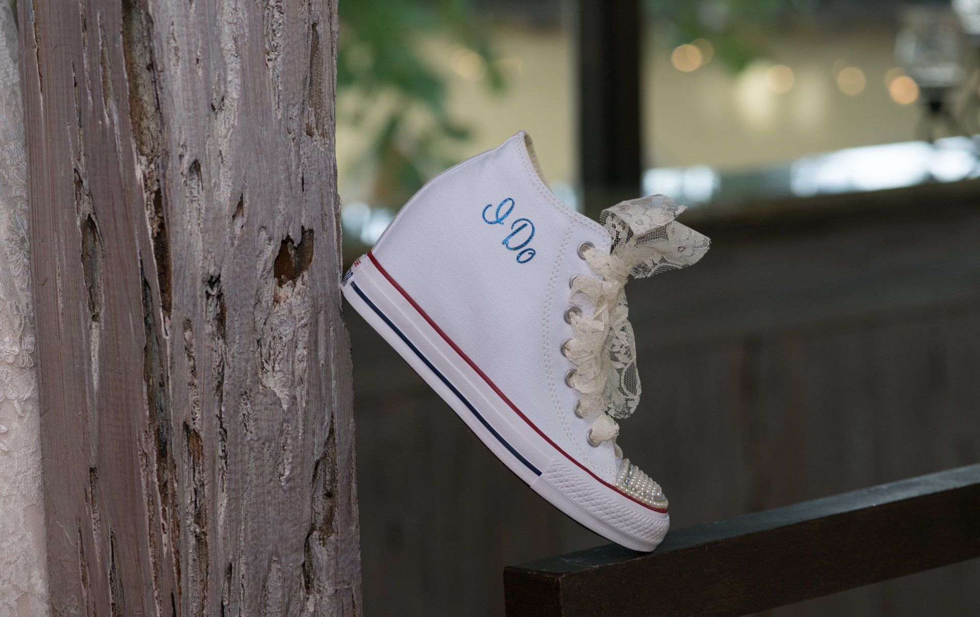 A pair of white converse shoes with monograms on them are hanging on a wooden post.